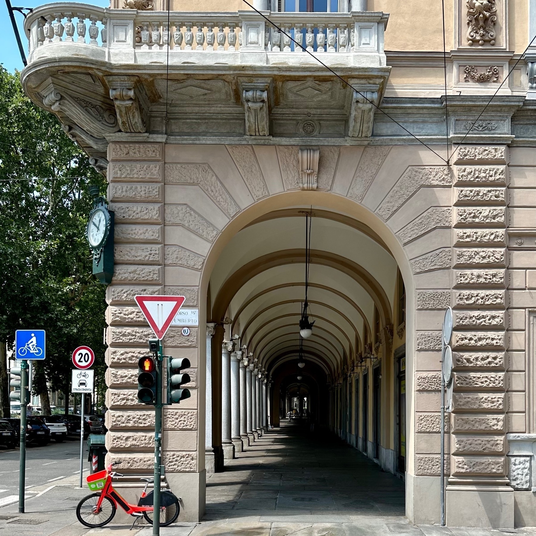 Looking across the street down the covered pedestrian walkway, appearing like a tunnel of arches, with a red public-use bicycle in the foreground