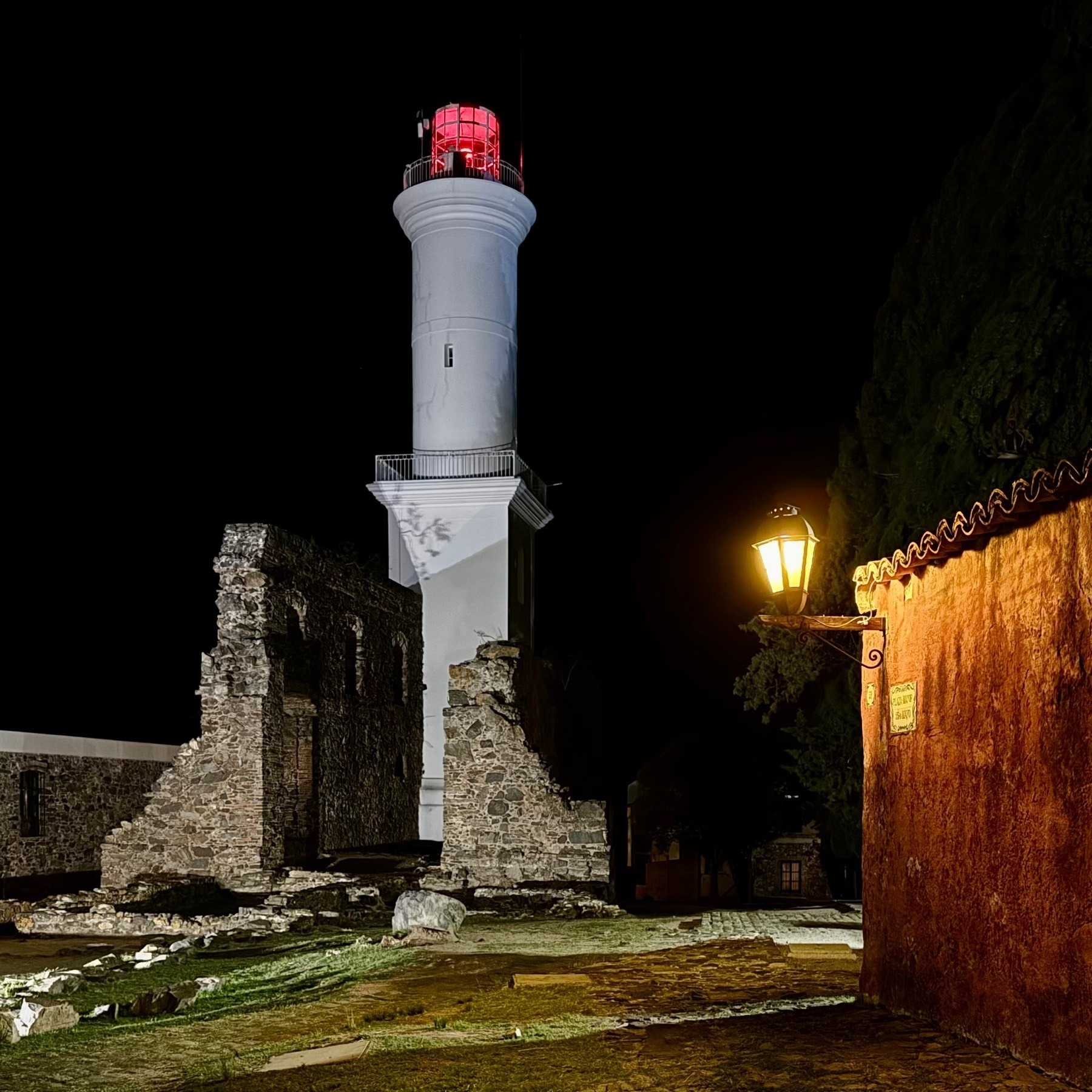 The Colonia del Sacramento Lighthouse with its red light shining, beside a renovated 18th-century Portuguese house, its lantern lit in yellow