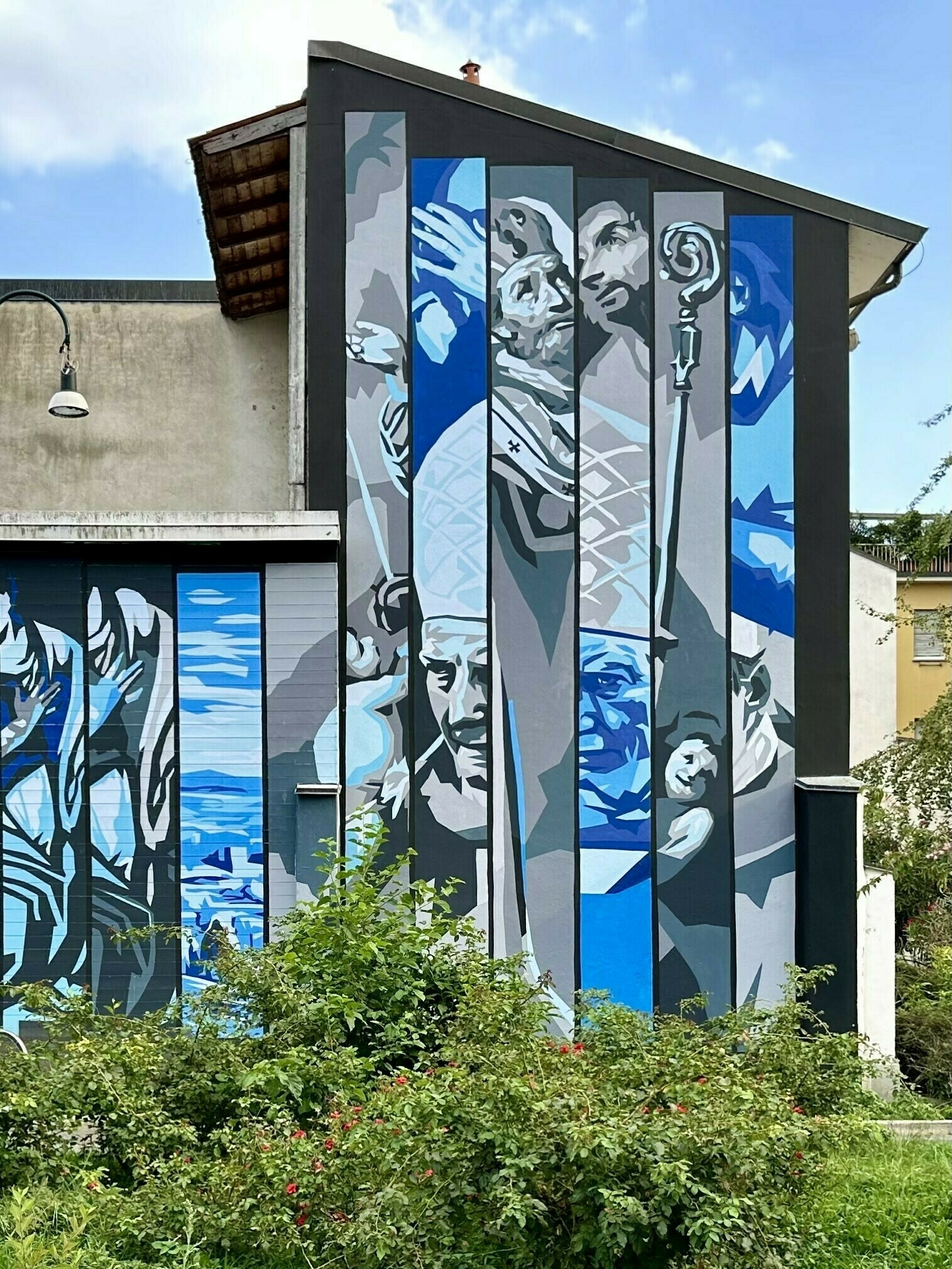 Striped mosaic of religious-subject murals in blue and grey on the side of a building