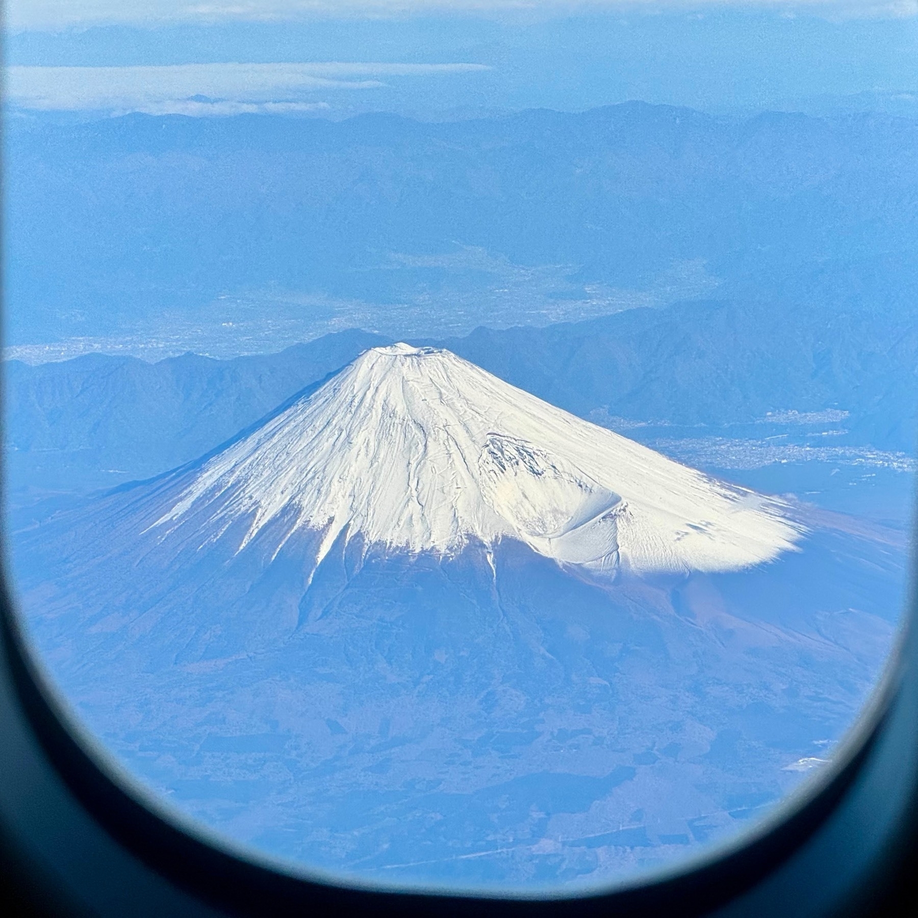 Snow-capped Mount Fuji with cloudless skies, taken through a plane window
