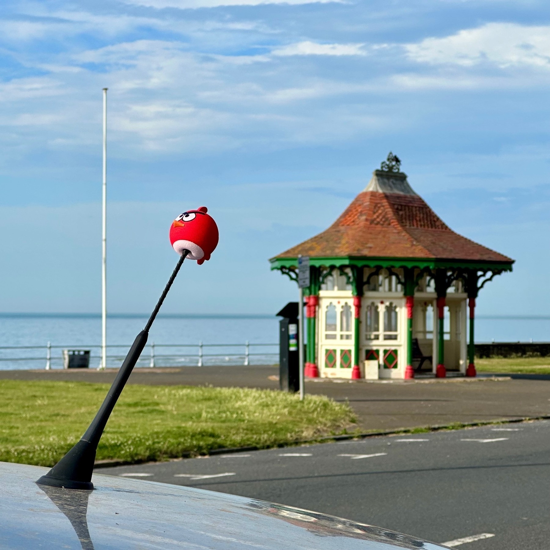 Red "Angry Bird" aerial topper on a car, in front of an old Victorian shelter on the promenade
