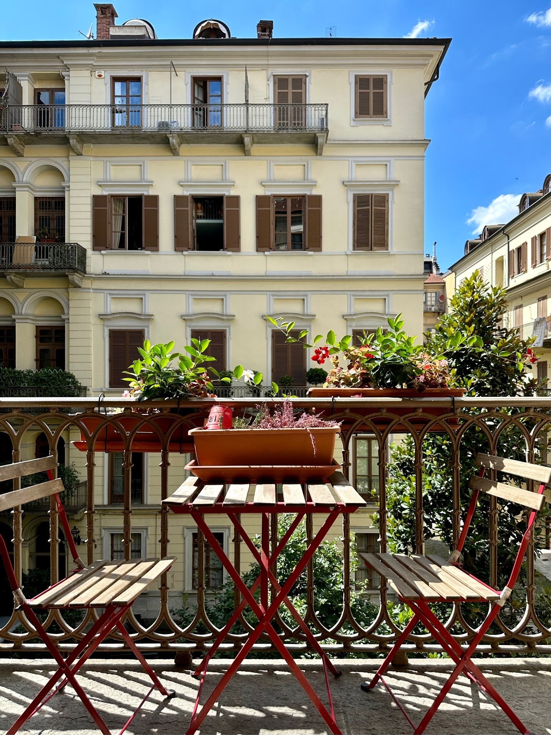 Two chairs and table on sunny balcony, looking out at Italian town houses