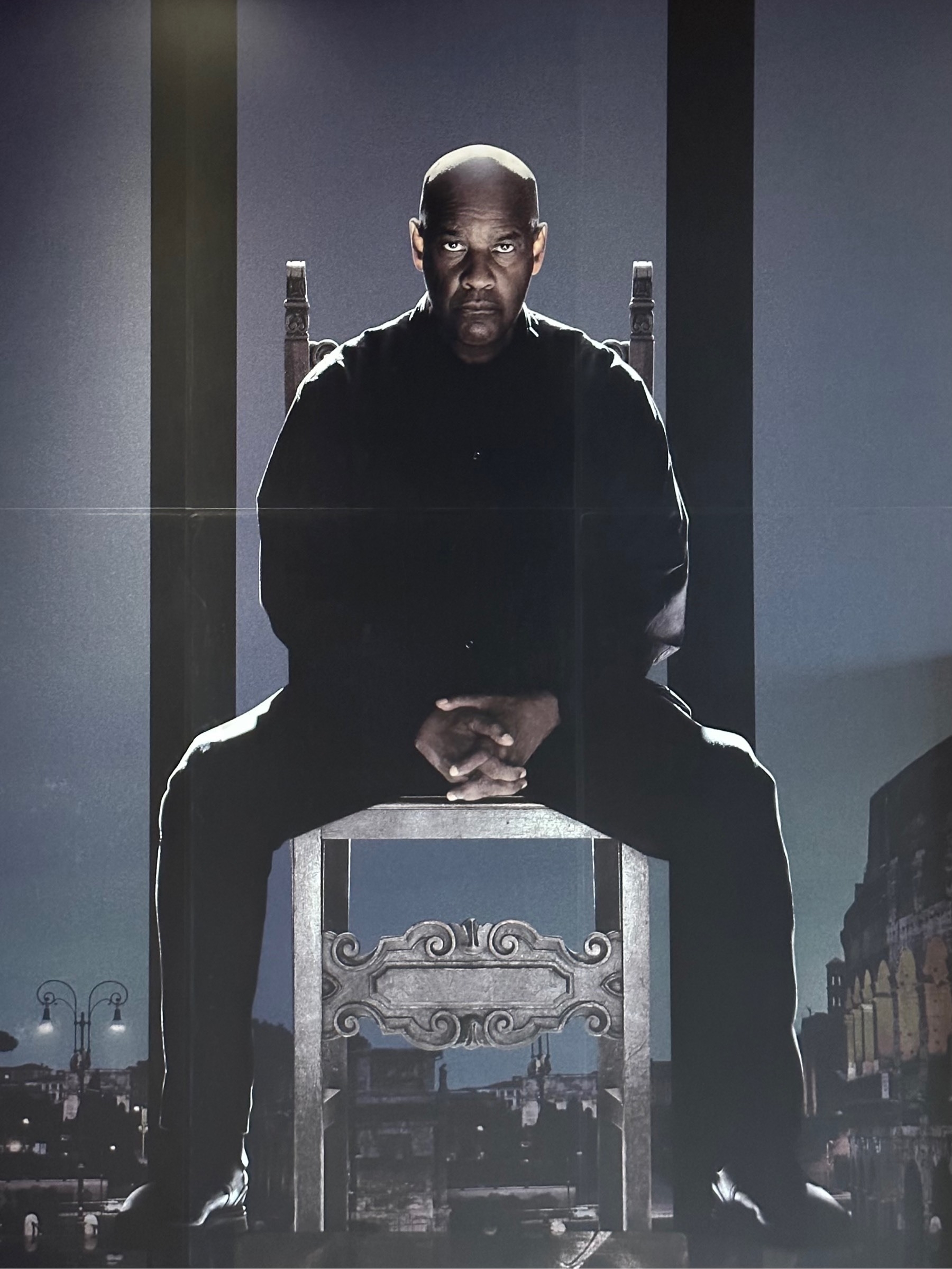 Denzel Washington dressed in black, sitting on a chair, eyes staring straight out, seeming like they're almost glowing; a poster for The Equalizer 3