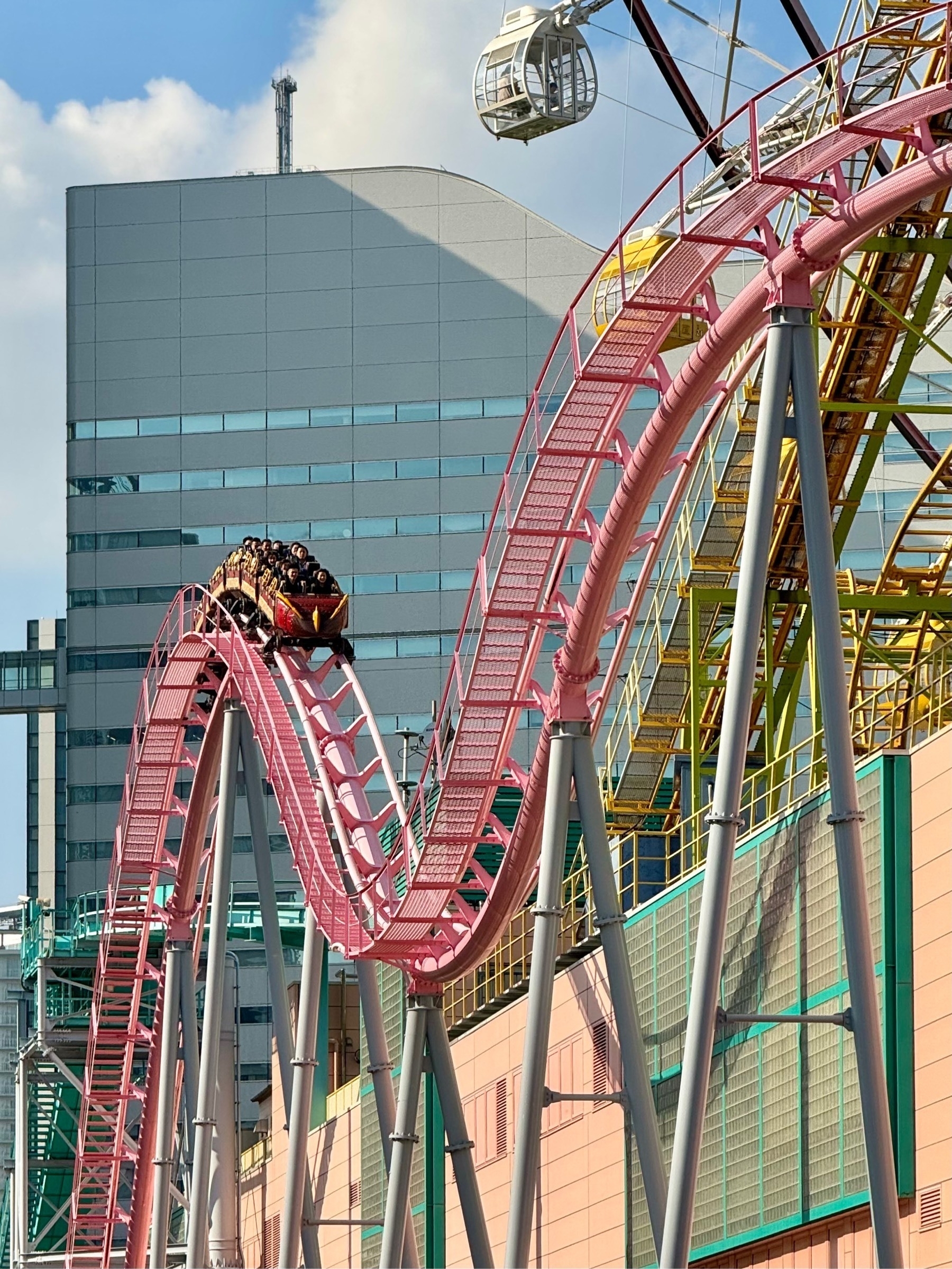 An M-shaped loop of the red Yokohama Cosmo World rollercoaster, with cars full of riders coming over the top of the first crest