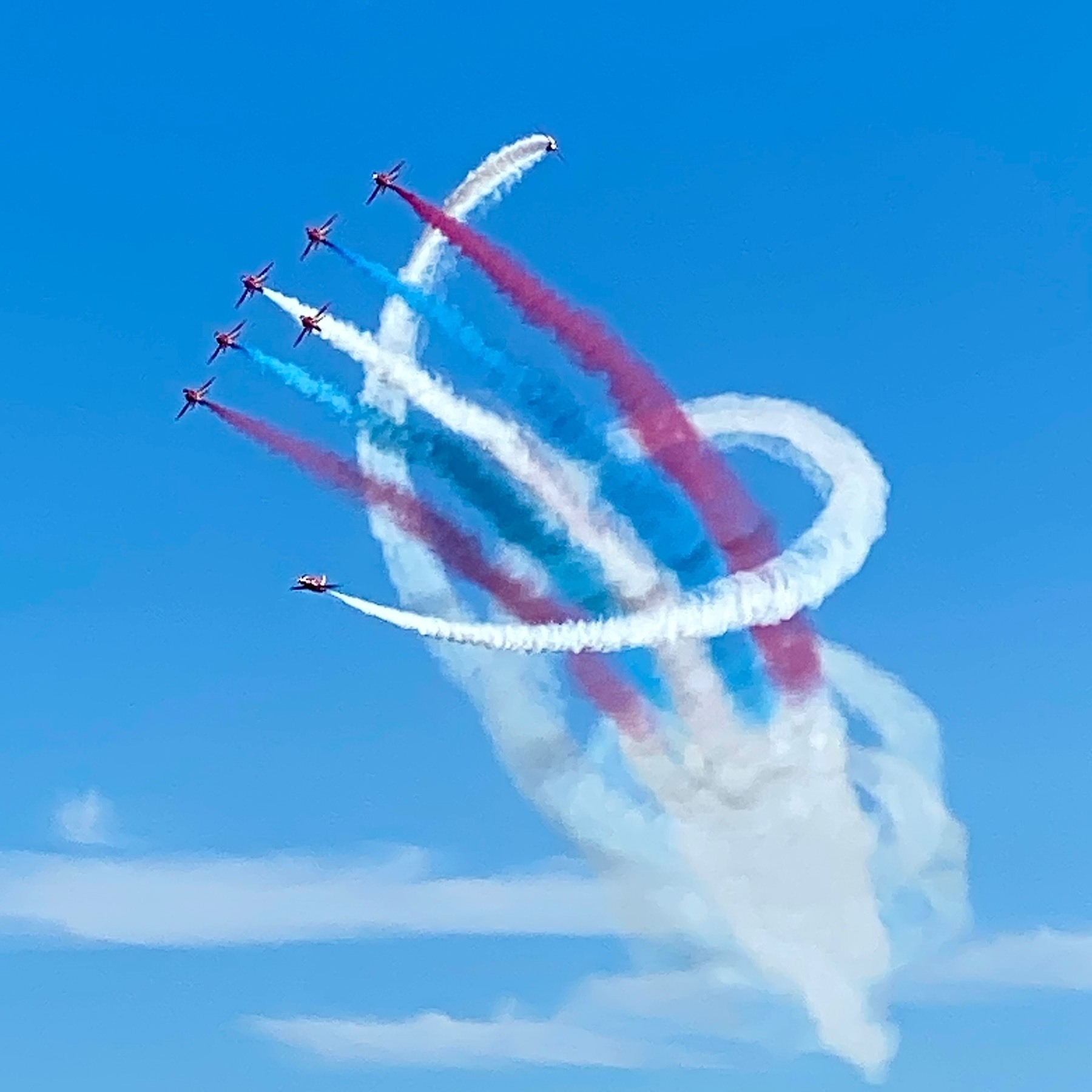 Flying formation; six planes in the middle, two emitting red smoke, two blue, one white, with two more flying round them in a corkscrew emitting white smoke
