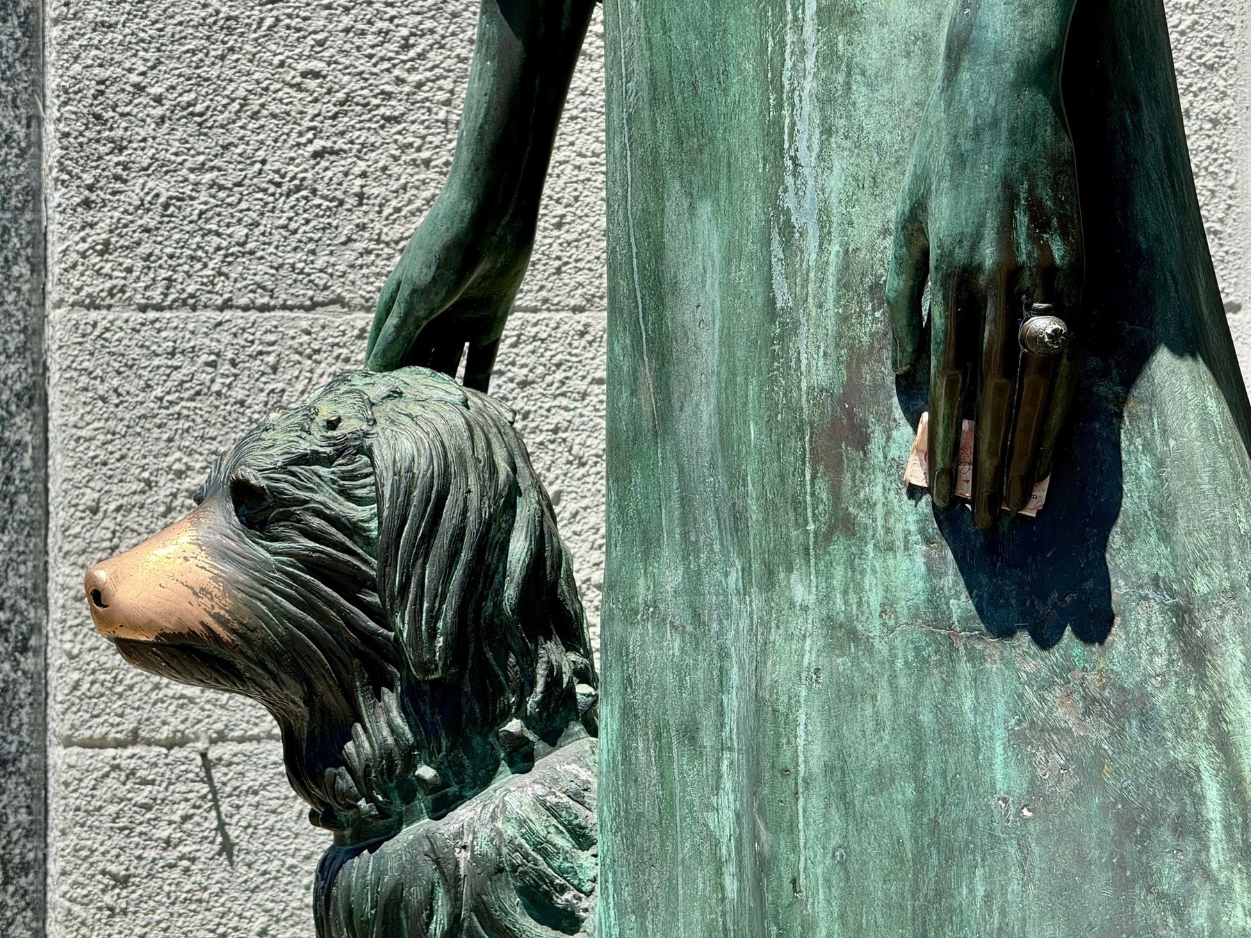 Section of a green-aged copper statue, of a young lady with her dog; the dog's nose rubbed clean, some money stuffed into her hand, her wedding ring very prominent. She is Liliana Crociati de Szaszak.
