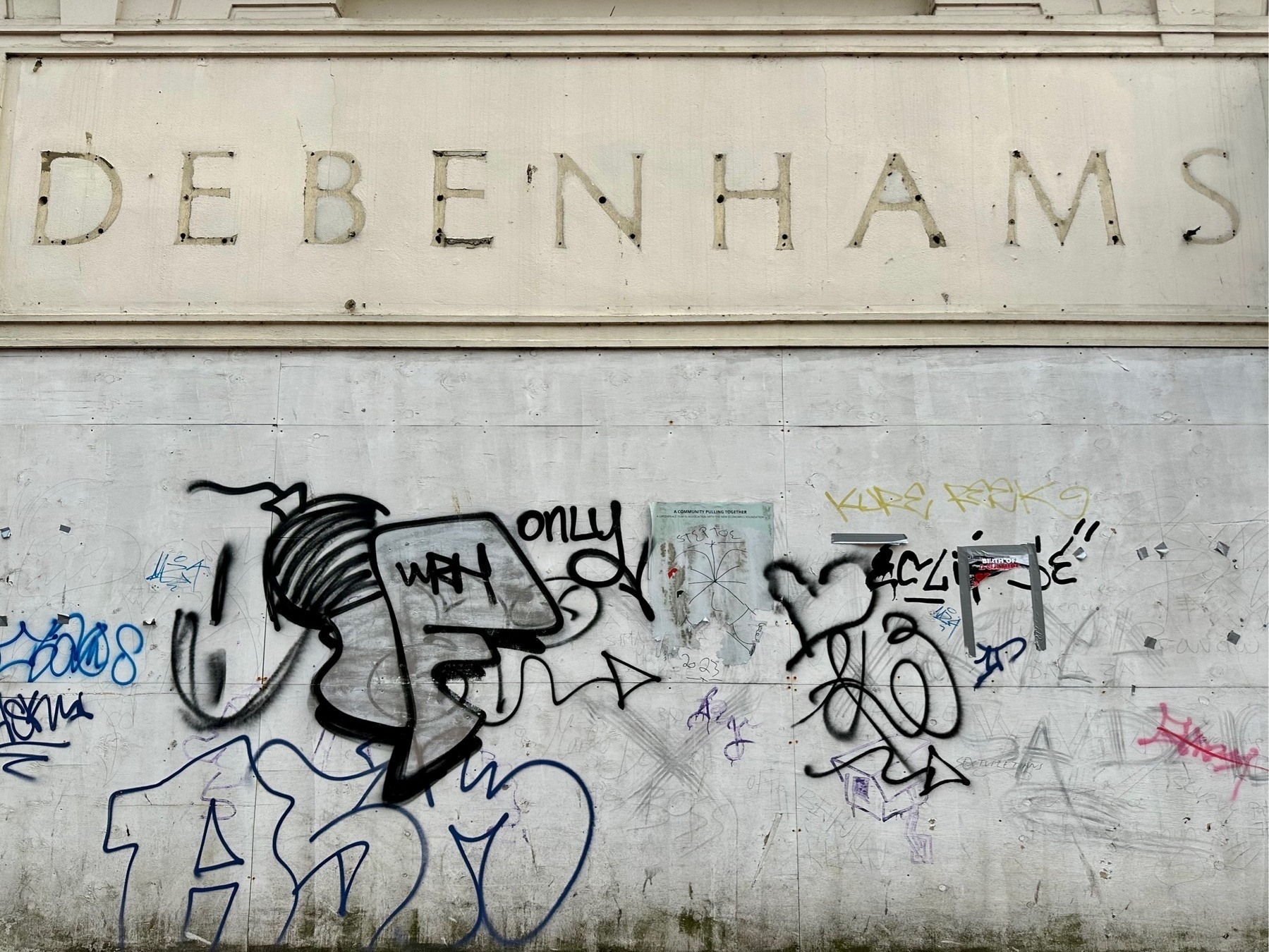 The indented letters making up an old Debenhams shop sign, with graffiti on the boards covering the old windows below