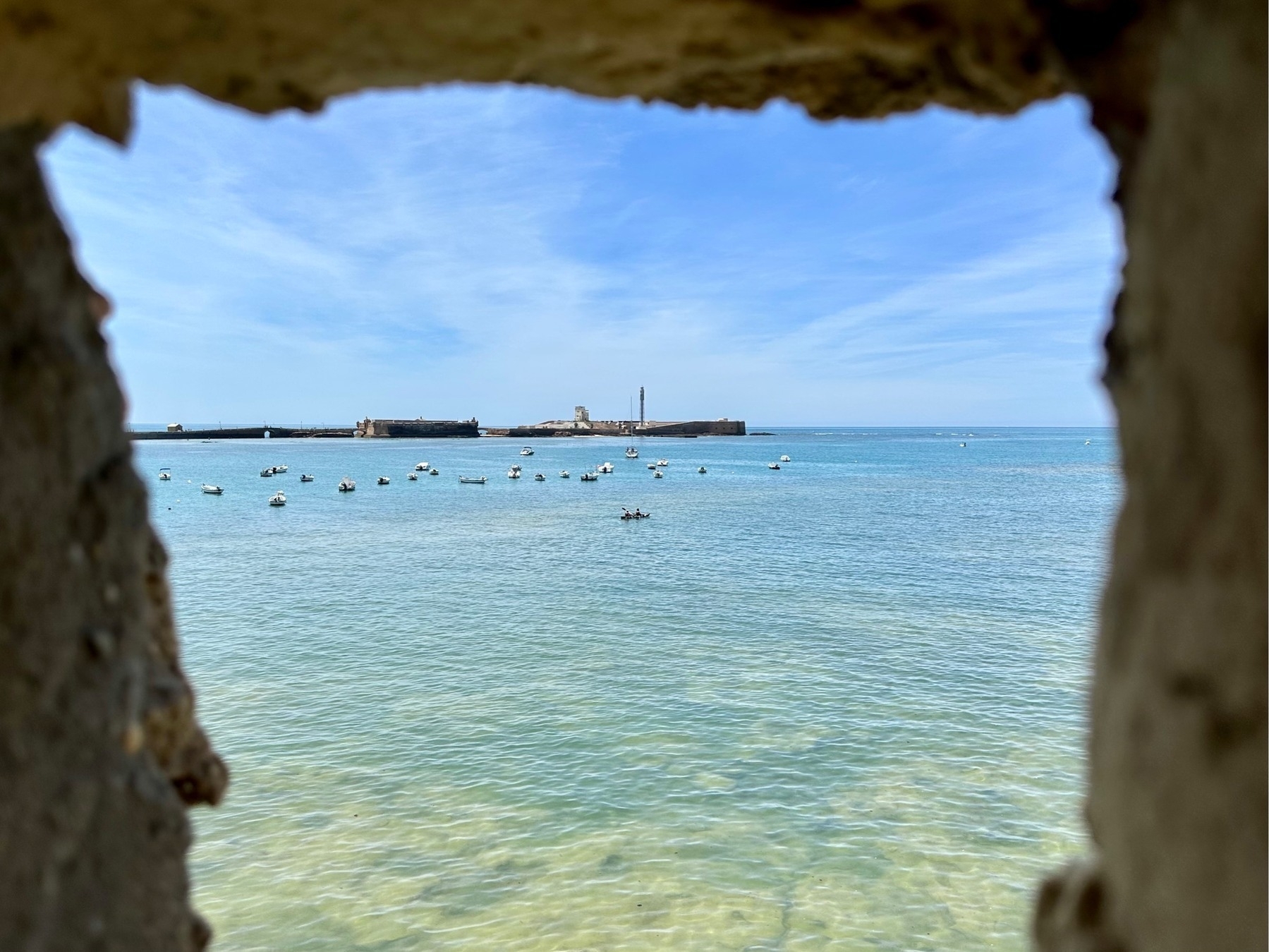 Looking out into the harbour through the frame of a castle embrasure, towards many anchored watercraft, and a small boat being rowed by two people