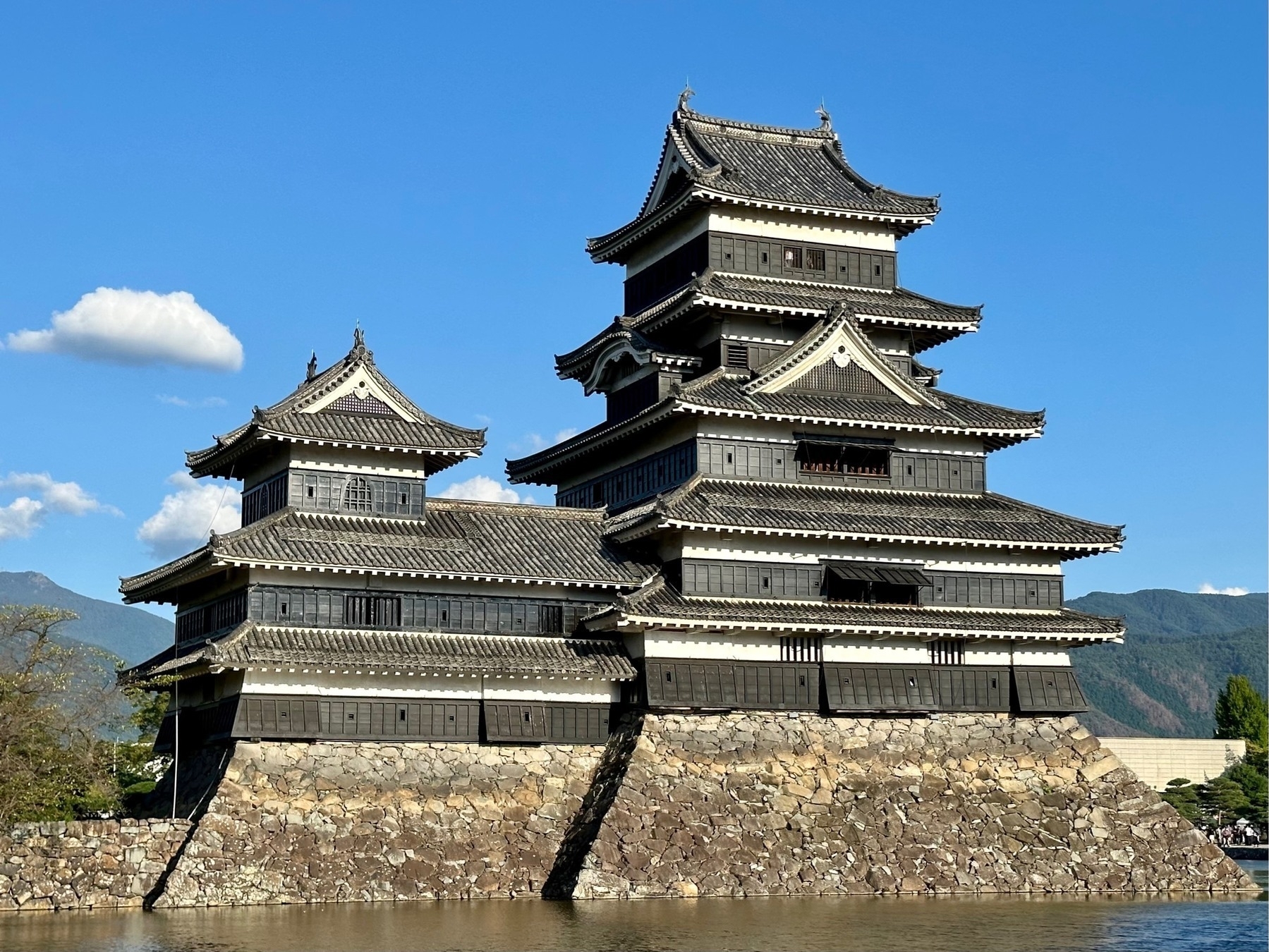 Japanese castle across its moat, set against a blue sky with a single cloud