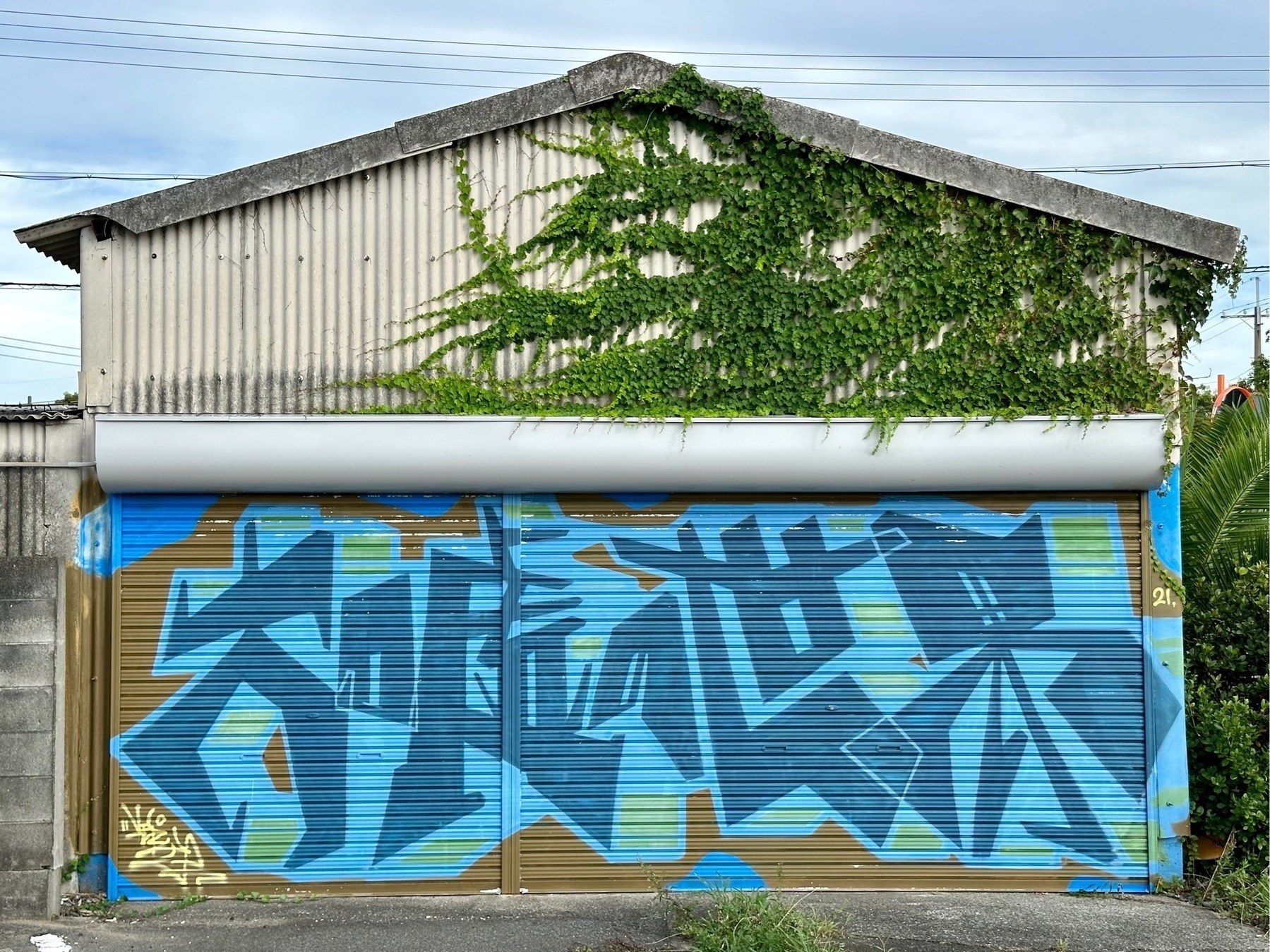 Mural on the side of a small warehouse building, consisting of five large blue stylised Japanese characters
