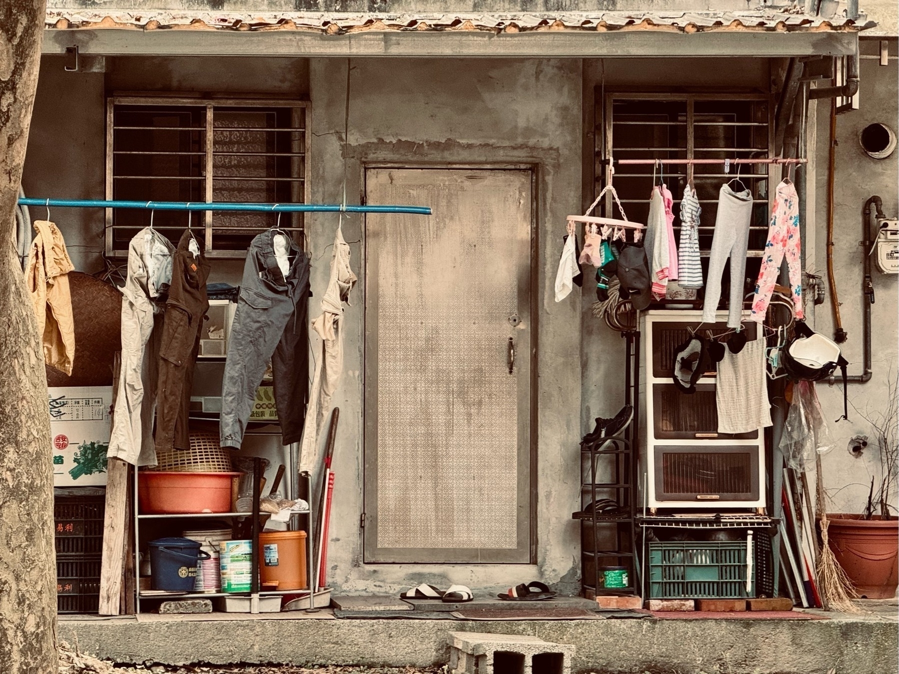 The front door of an old and tired single-storey abode with washing hanging out front on both sides, flip-flops on the doorstep. A scene perhaps hard to age