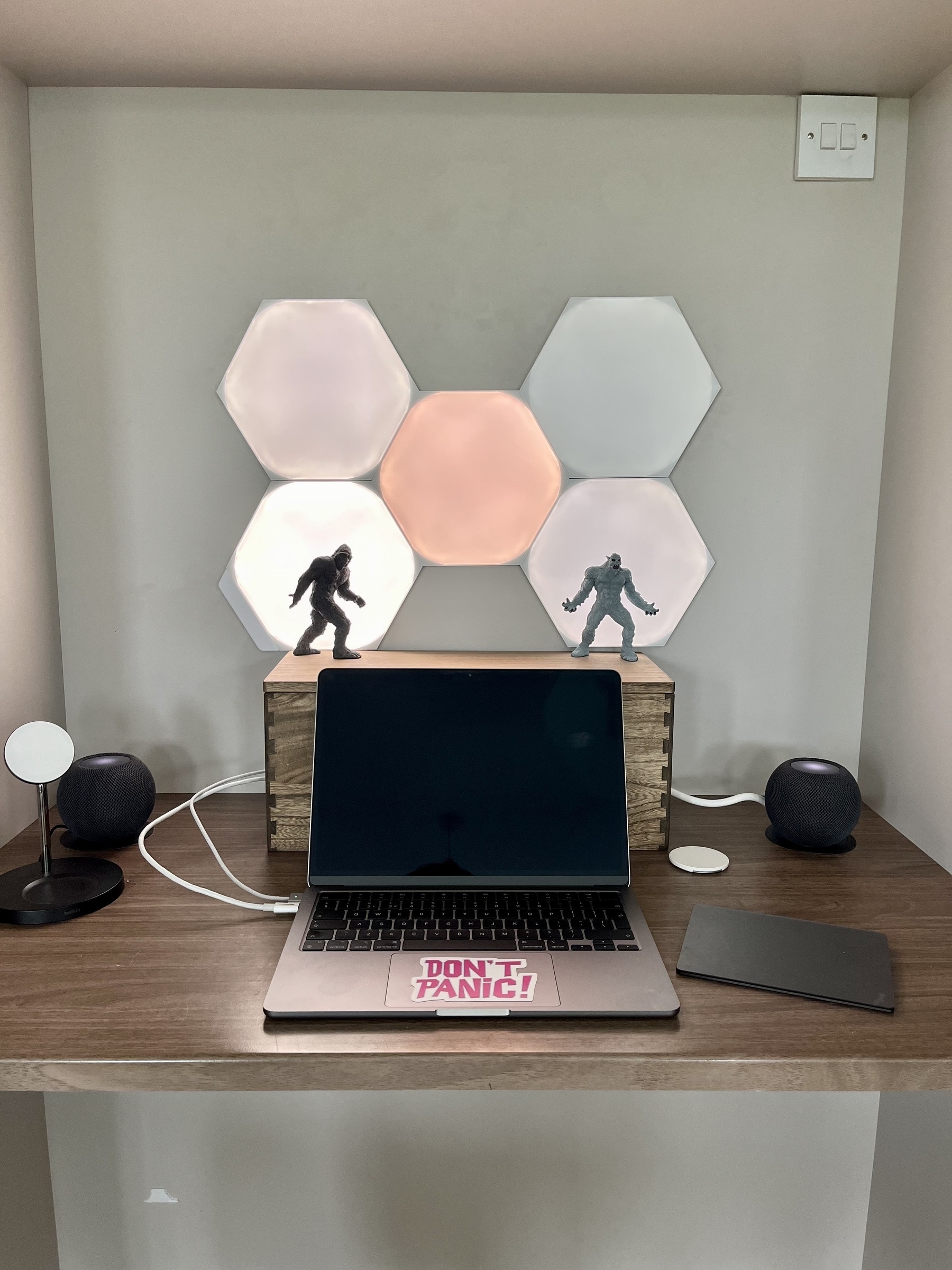 A MacBook computer sits below a wooden box, perched on which is a Sasquatch and yeti figure illuminated against lights. Circular HomePods sit each side of the box. 
