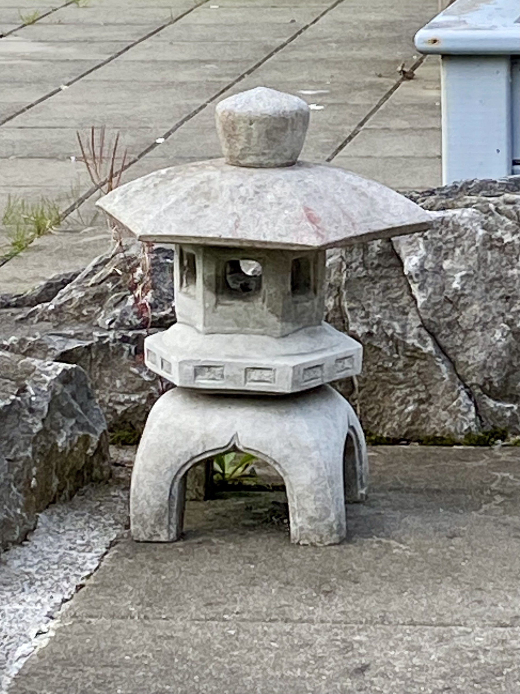 A Japanese pergola ornament sitting in front of stone. 