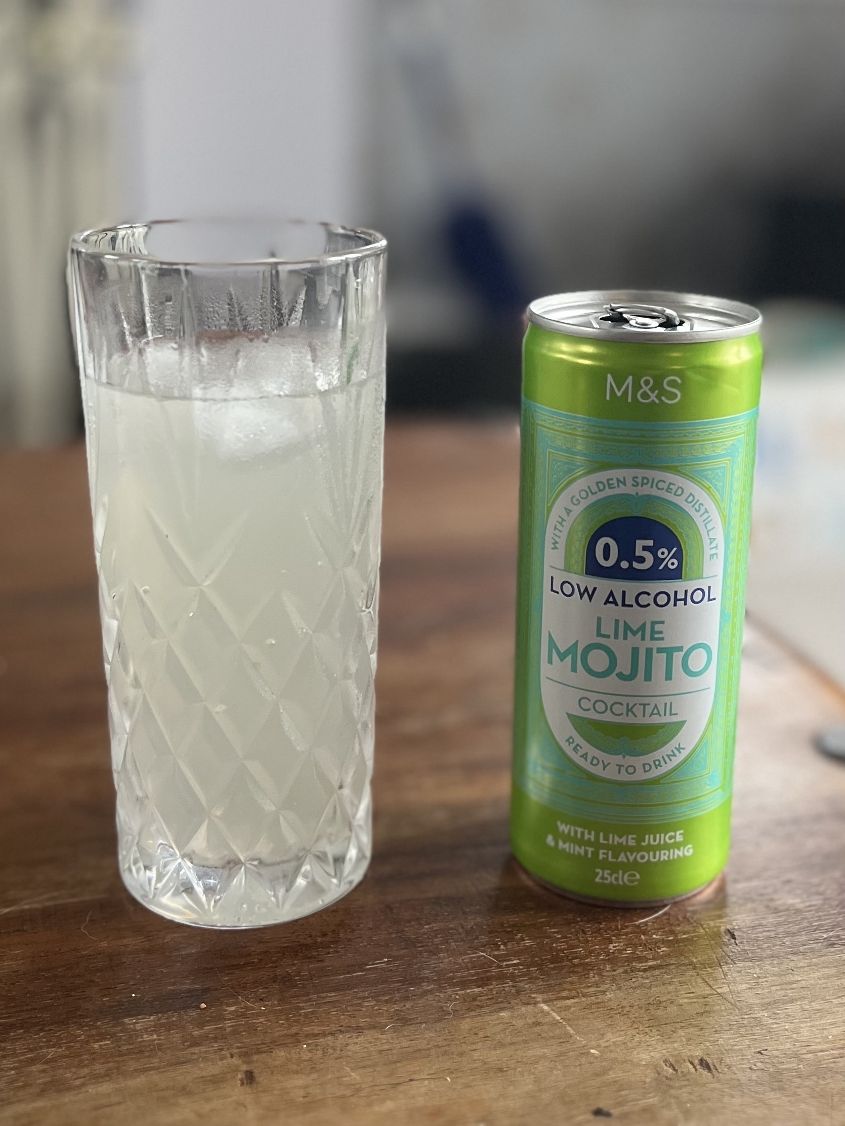 A glass of cloudy liquid and a green can of low alcohol lime mojito. 