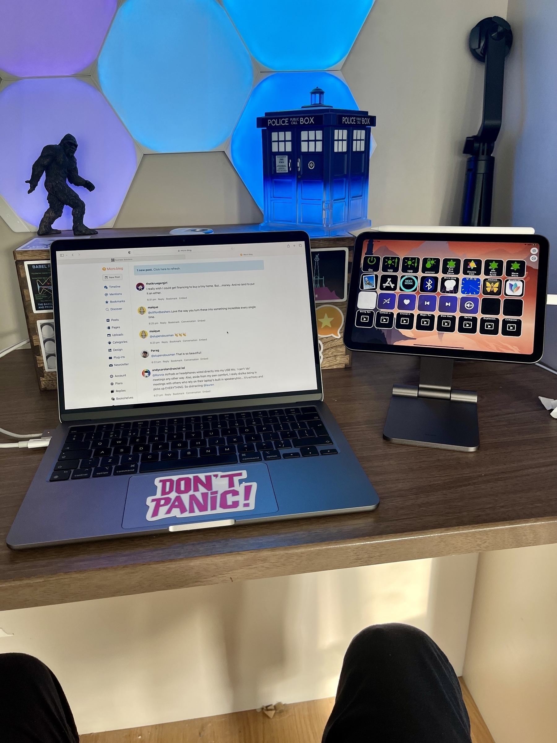 A MacBook Air sits beside a raised iPad Mini. Behind a TARDIS police-box and sasquatch are illuminated in blue and mauve. 