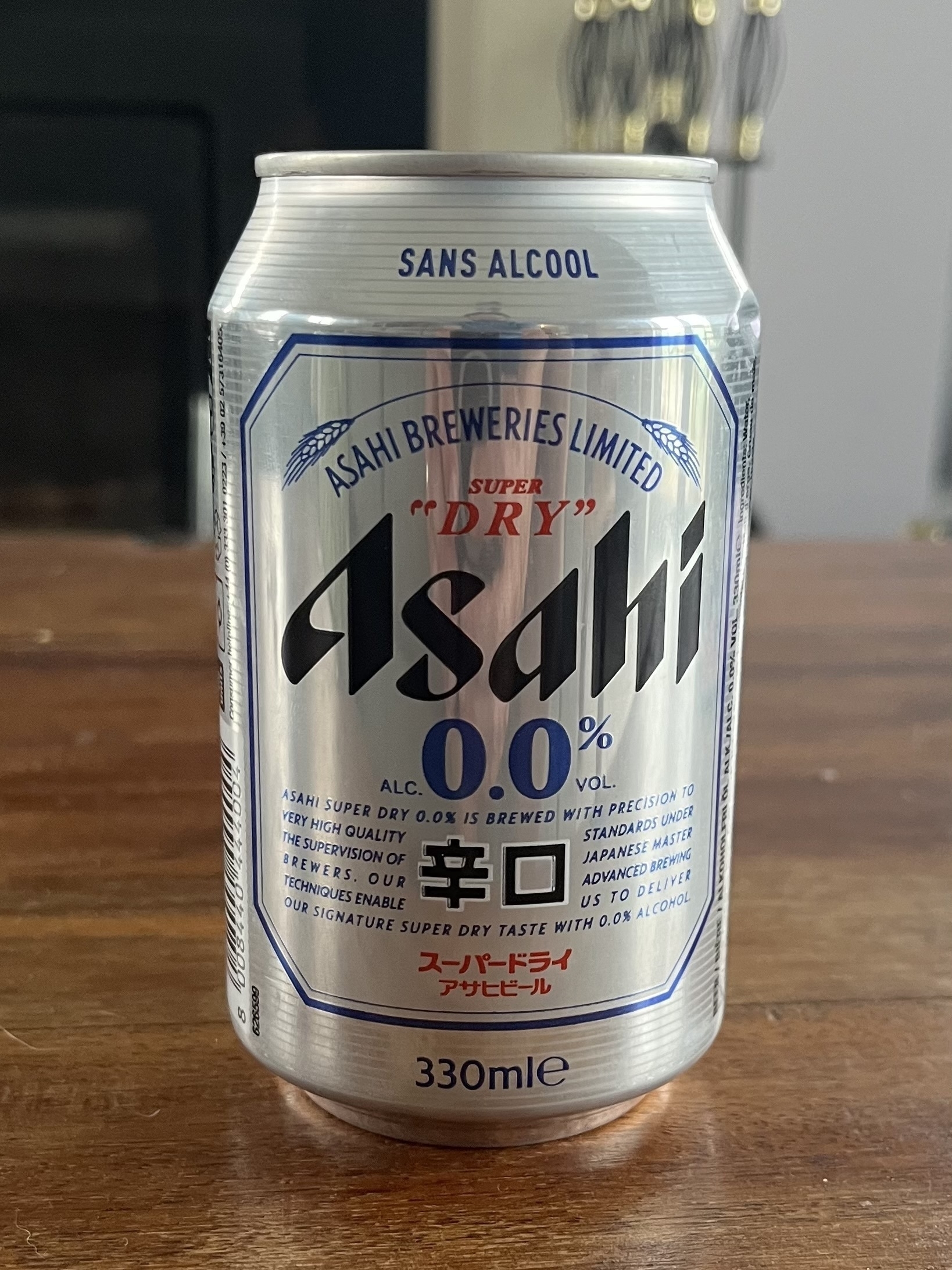 A silver can of Asahi 0% beer sits unopened on a brown table. 