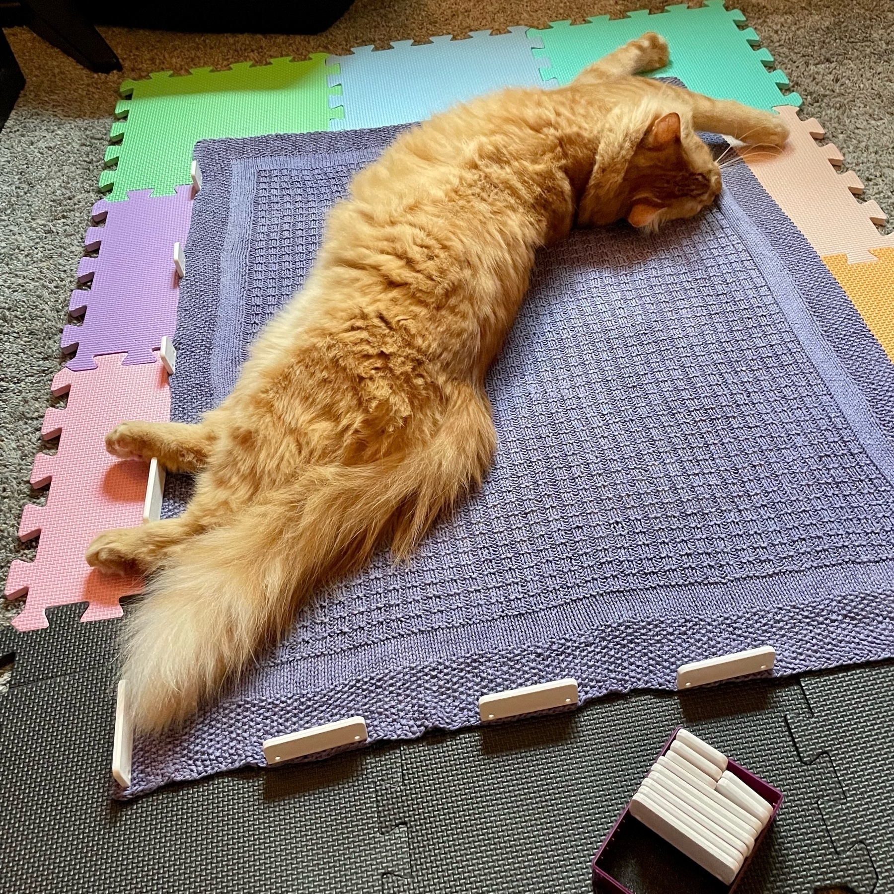 large orange cat stretched out on knitted blanket 