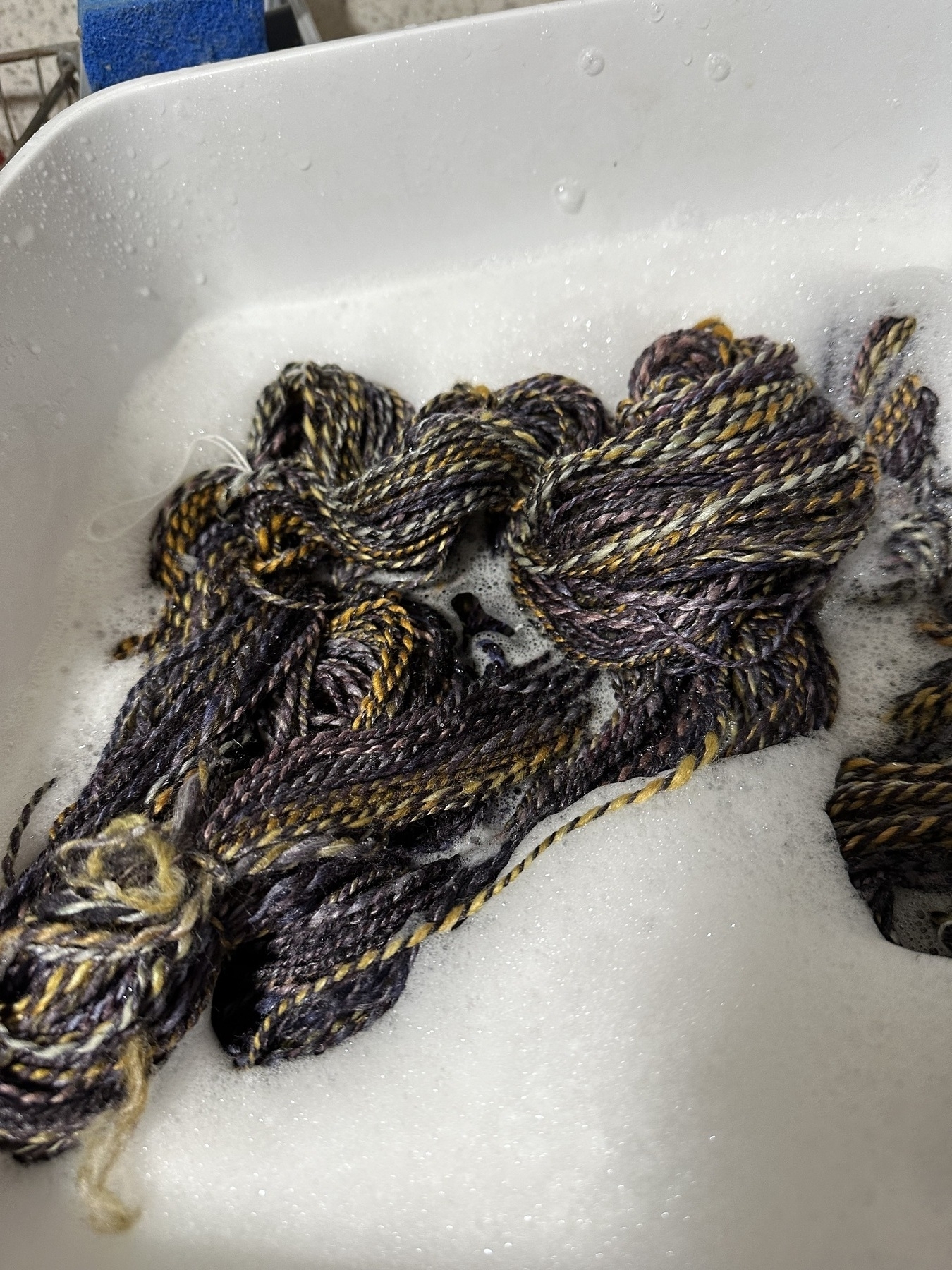 dark blue and gold two-ply handspun yarn going into soapy water