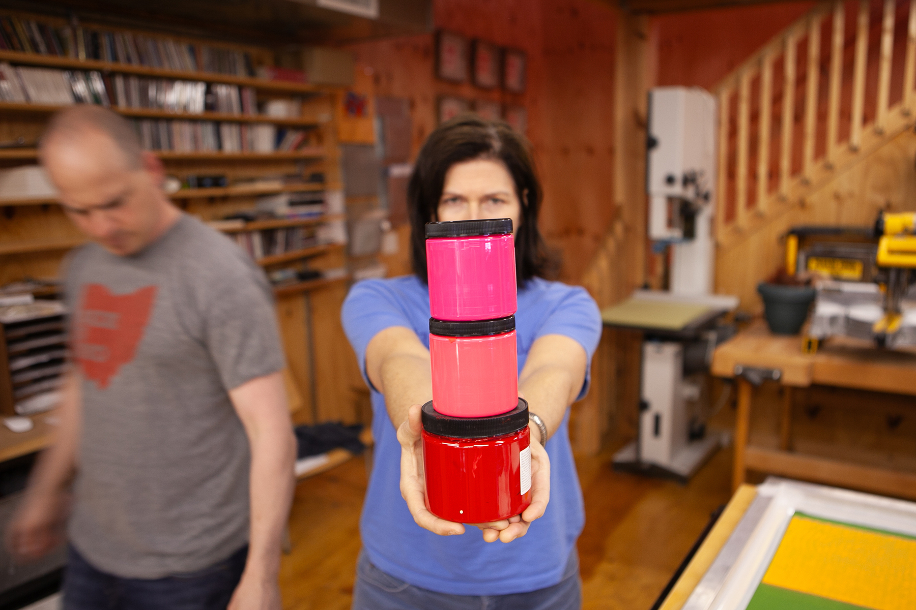 Woman holds up three jars of screen printing inks, hot pink, pink and red - Canon 5D Mark II