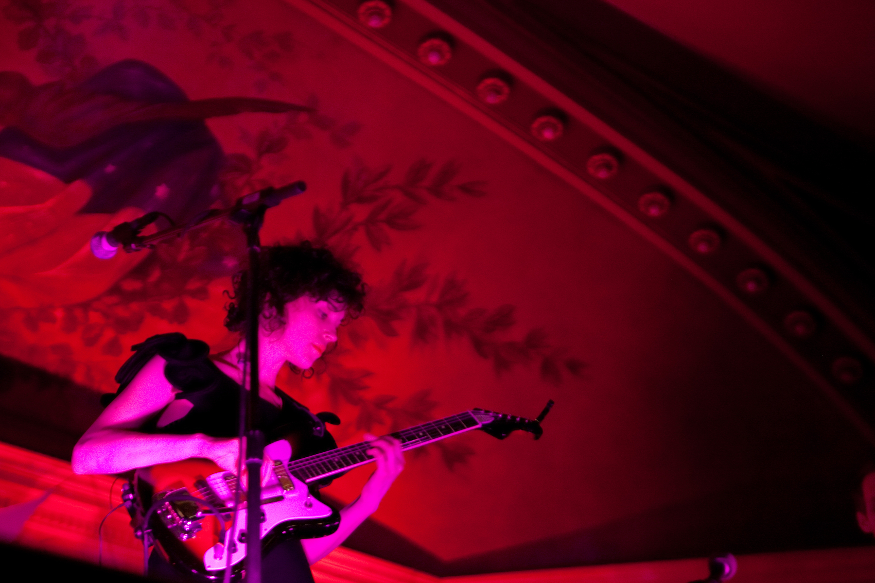 Annie Clark, bathed in magenta light against a stage in red light plays a guitar - Canon EOS 5D Mark II