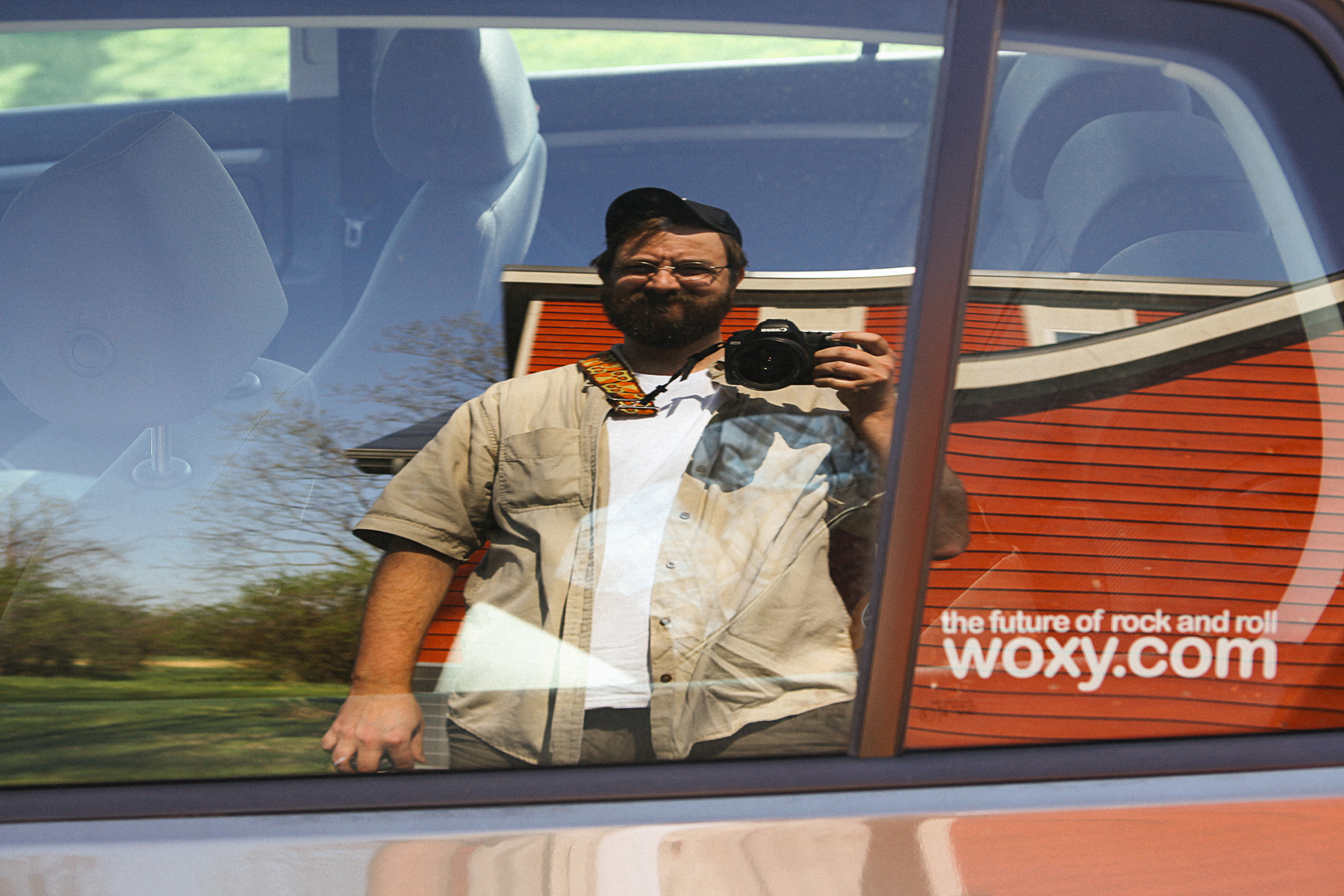 Man takes selfie in reflection of car window with a sticker that reads "woxy.com the future of rock and roll" - Canon 5D Mark II