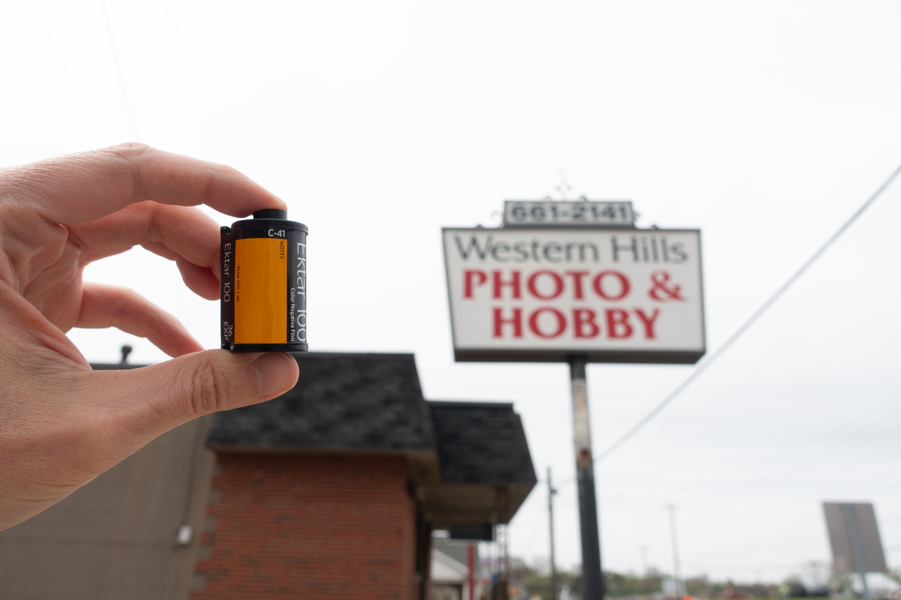 Person holding a roll of Kodak Ektar 100 film in front of a sign for Western Hills Photo & Hobby - Sony RX100