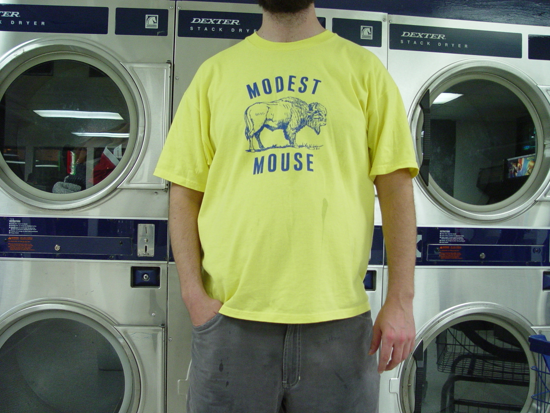 Man in yellow MODEST MOUSE t-shirt with buffalo graphic in front of industrial washing machines - Sony CyberShot