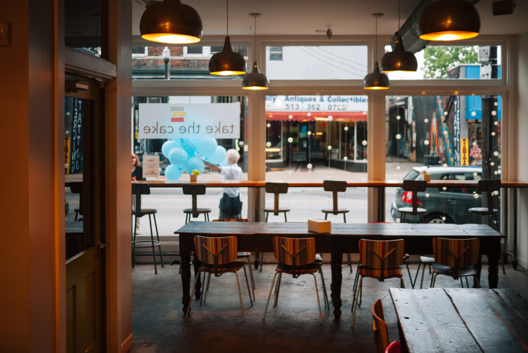 Blurry photo of cafe. Outside the window a woman is holding a bunch of teal balloons - Panasonic Lumix GF1 