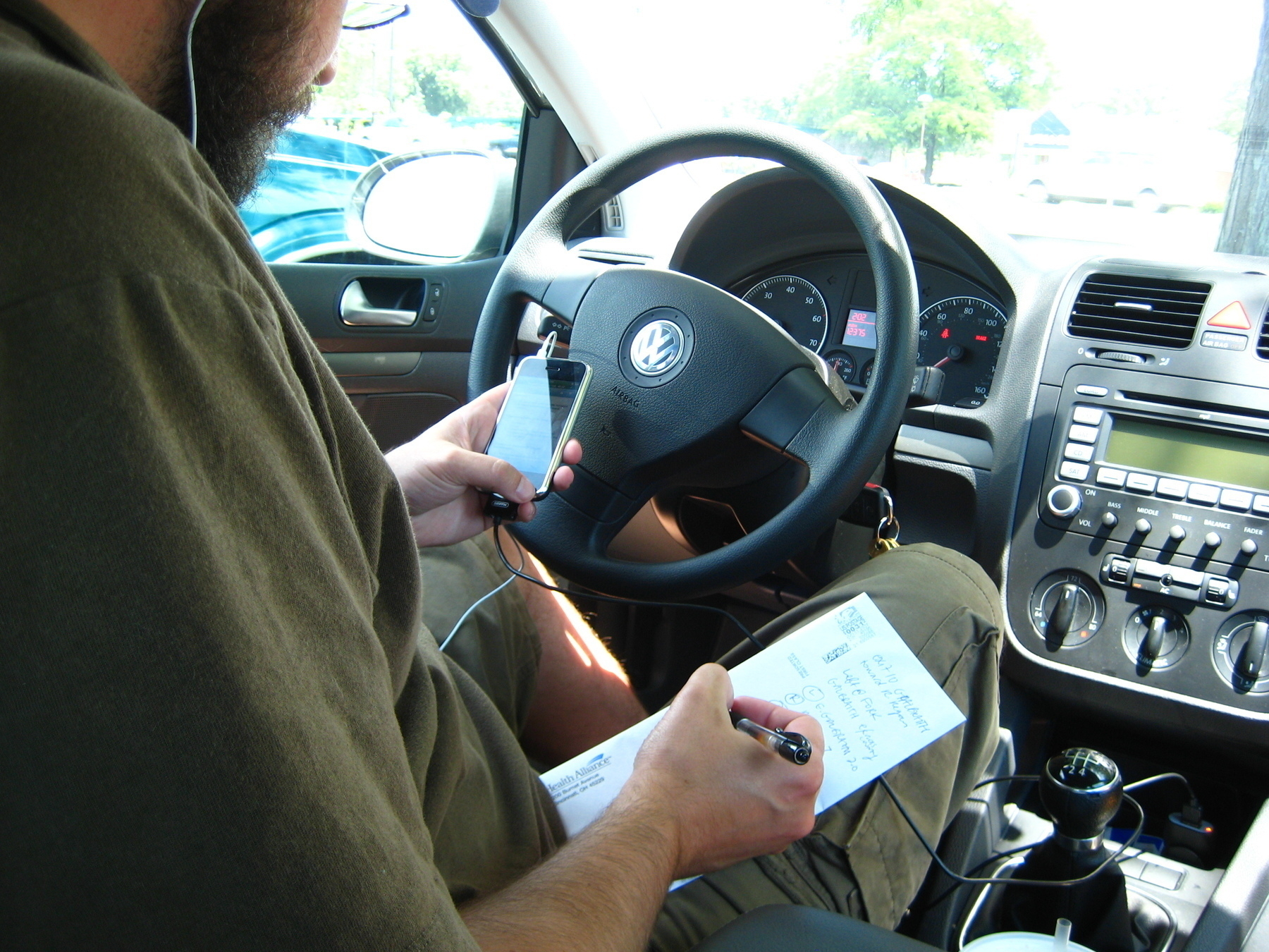 Bearded person on first gen iPhone in parked car writing directions on the back of an envelope - Canon PowerShot SD750