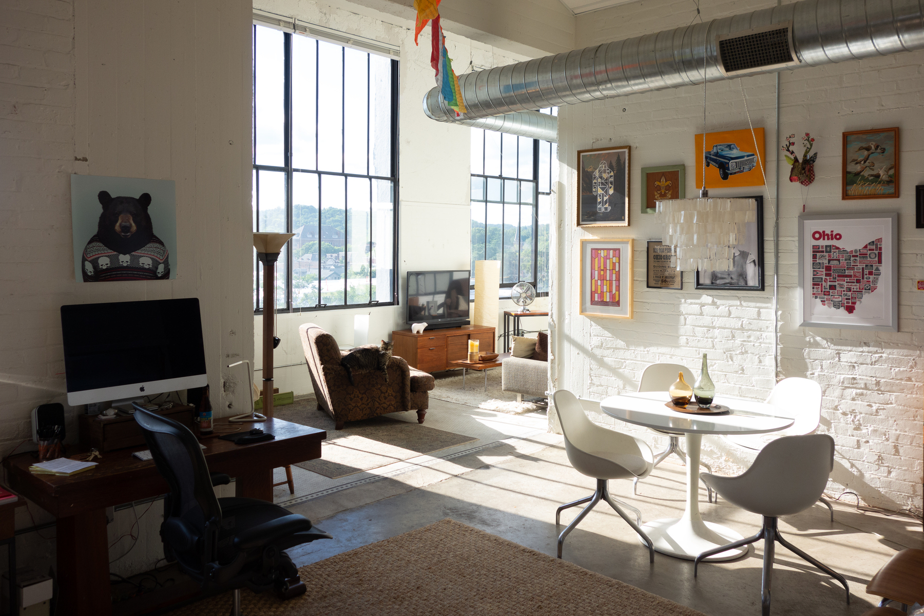 Warm light streams into a converted loft from a factory. A cat sits on the arm of a wide chair - Sony RX100