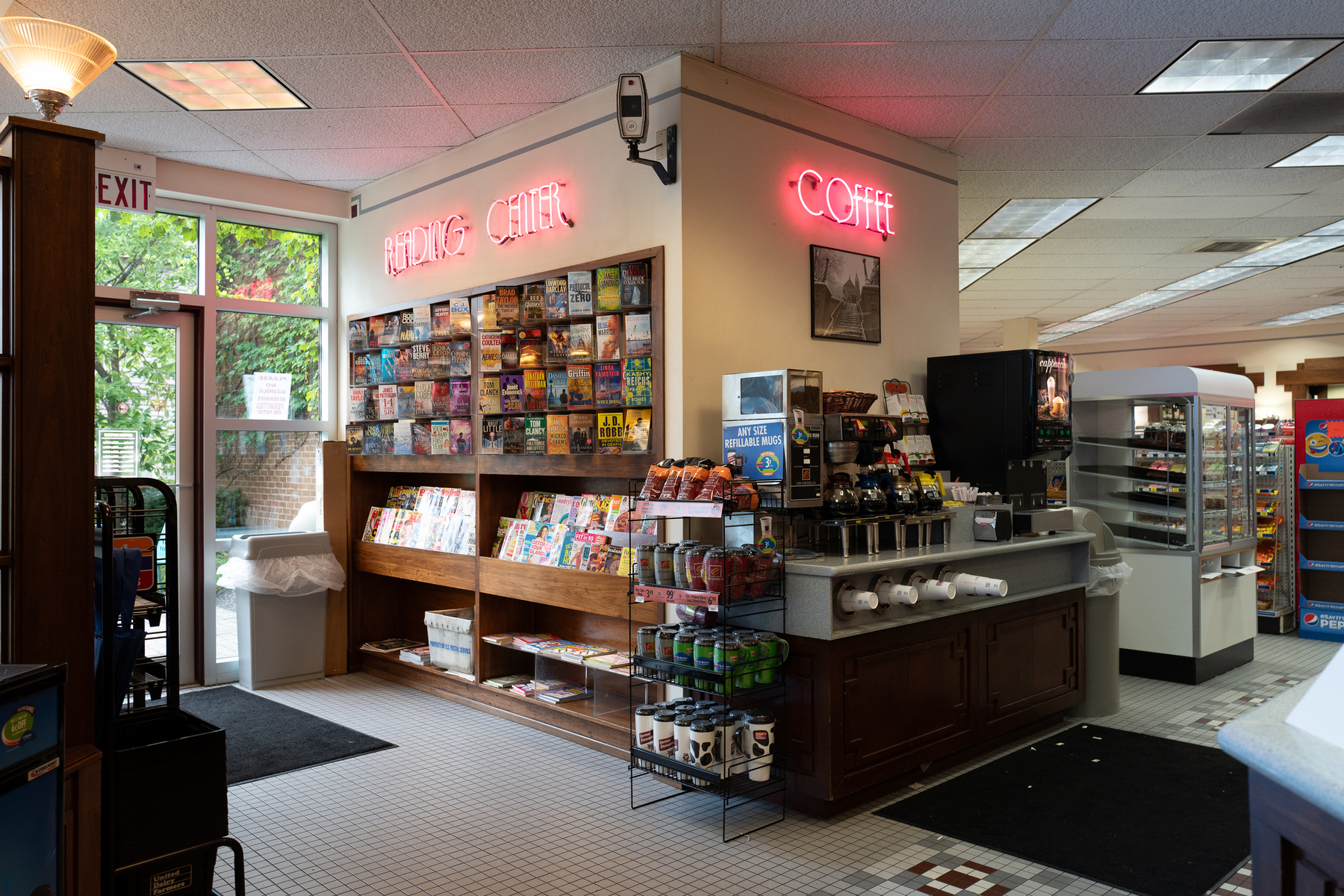 A rack of paperback books and magazines with a neon sign that says READING CENTER and a coffee station with a COFFEE neon sign at UDF - Leica Q