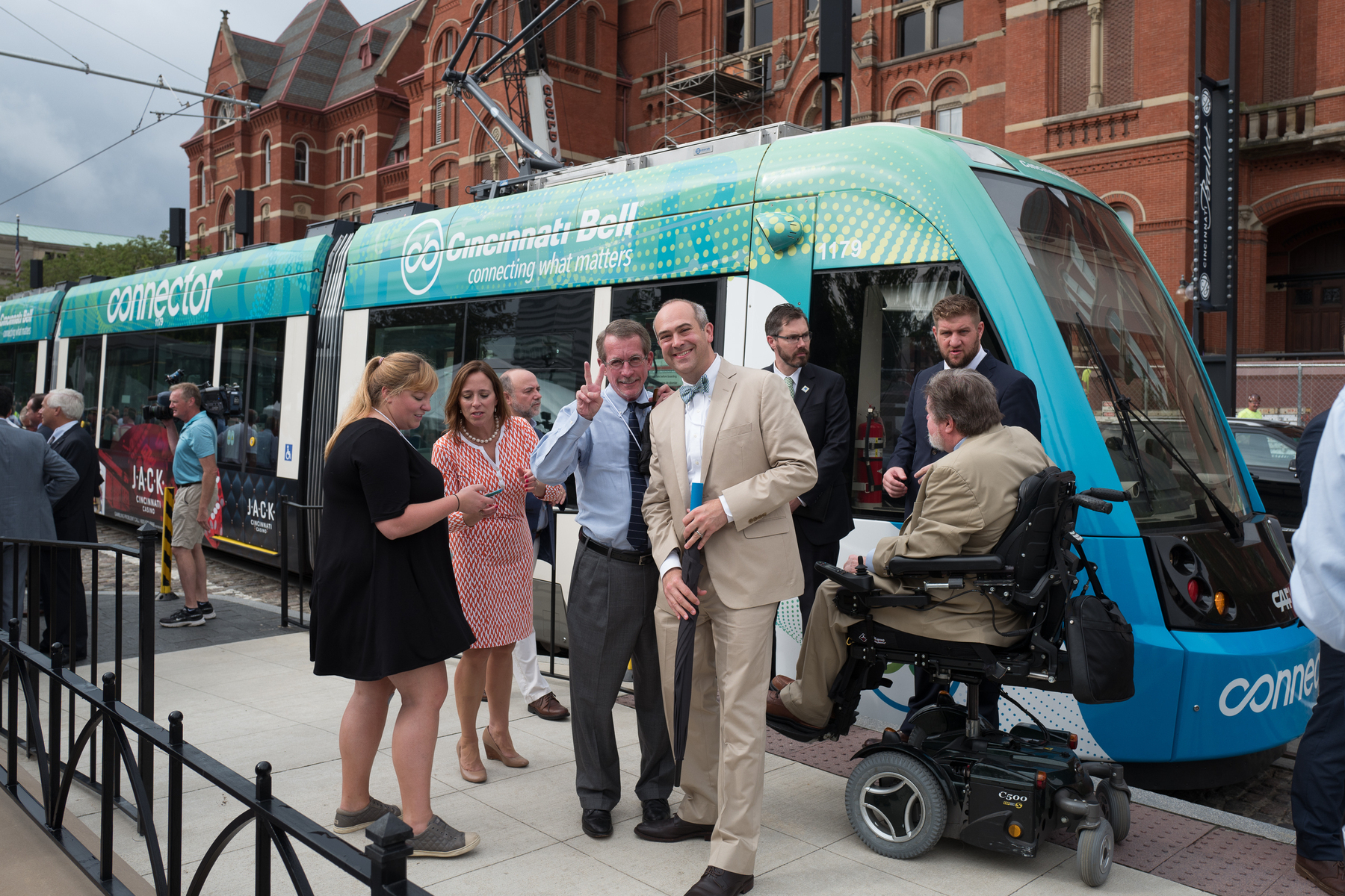 A group of folks, one giving a peace sign, stand in front of a shiny new streetcar in Cincinnati that became operational that day - Leica Q