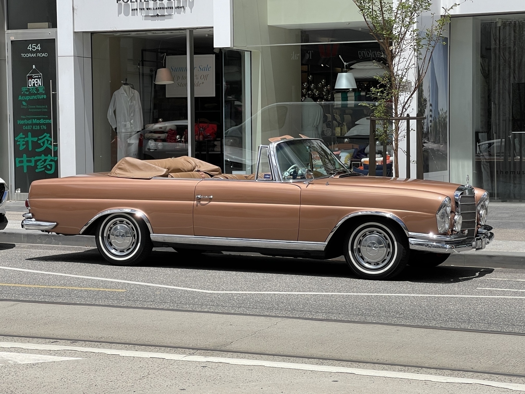 A copper coloured vintage Mercedes Benz 220 SE. Two door convertible with the top down.