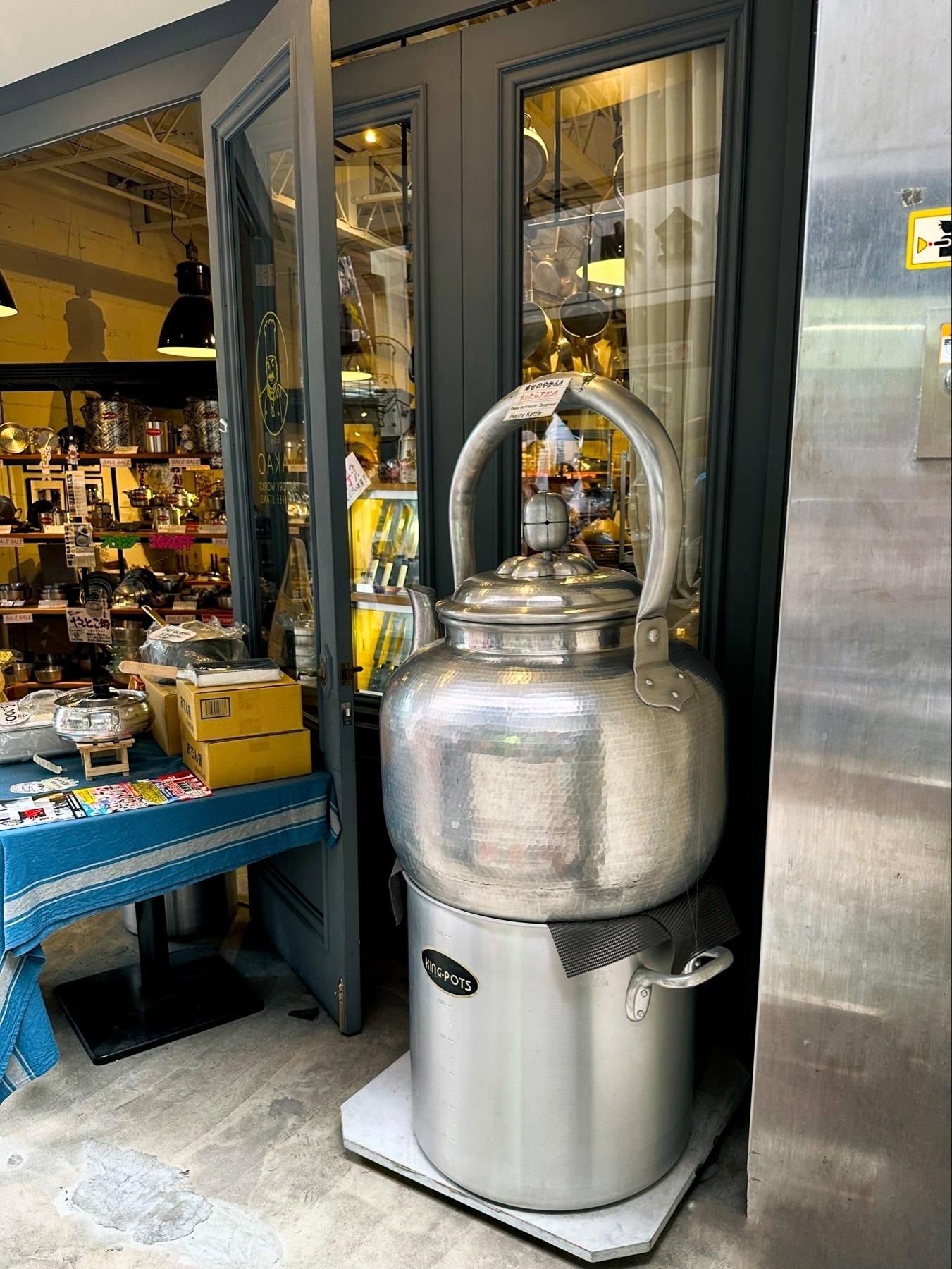 An oversized novelty teapot displayed outside a store, resembling a traditional stove-top kettle.