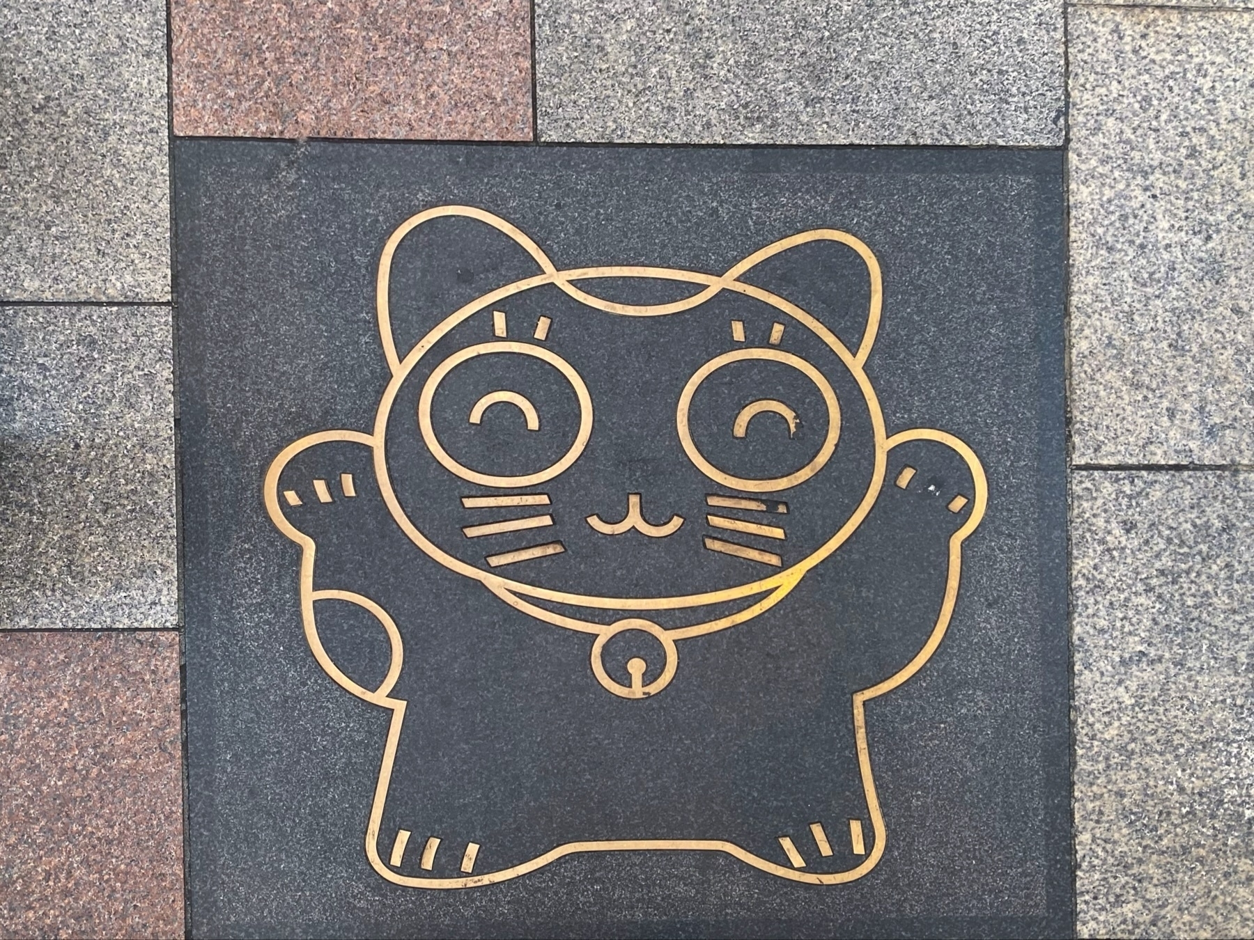 A maneki-neko (beckoning cat) design embedded in a pavement tile.