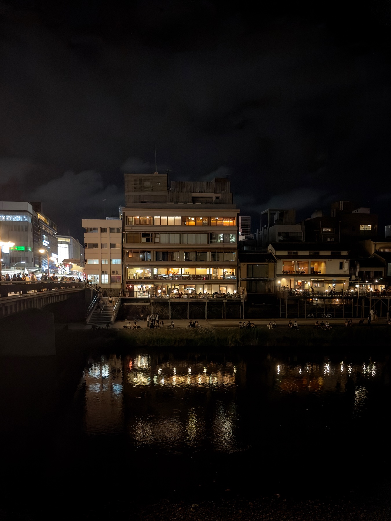 A row of riverside restaurants at night. The glow of the windows lighting and reflecting the water