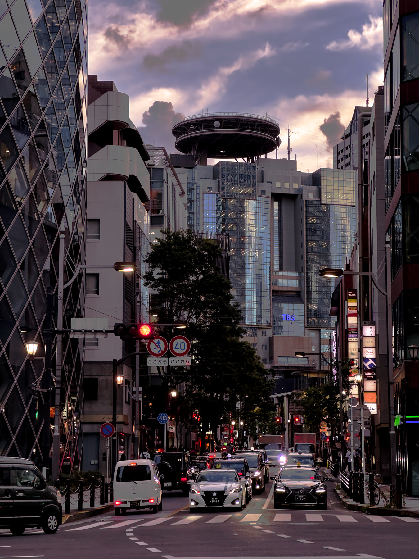 A portrait of a Tokyo street at sunset. Skyscrapers loom in the background with powerful looking clouds.
