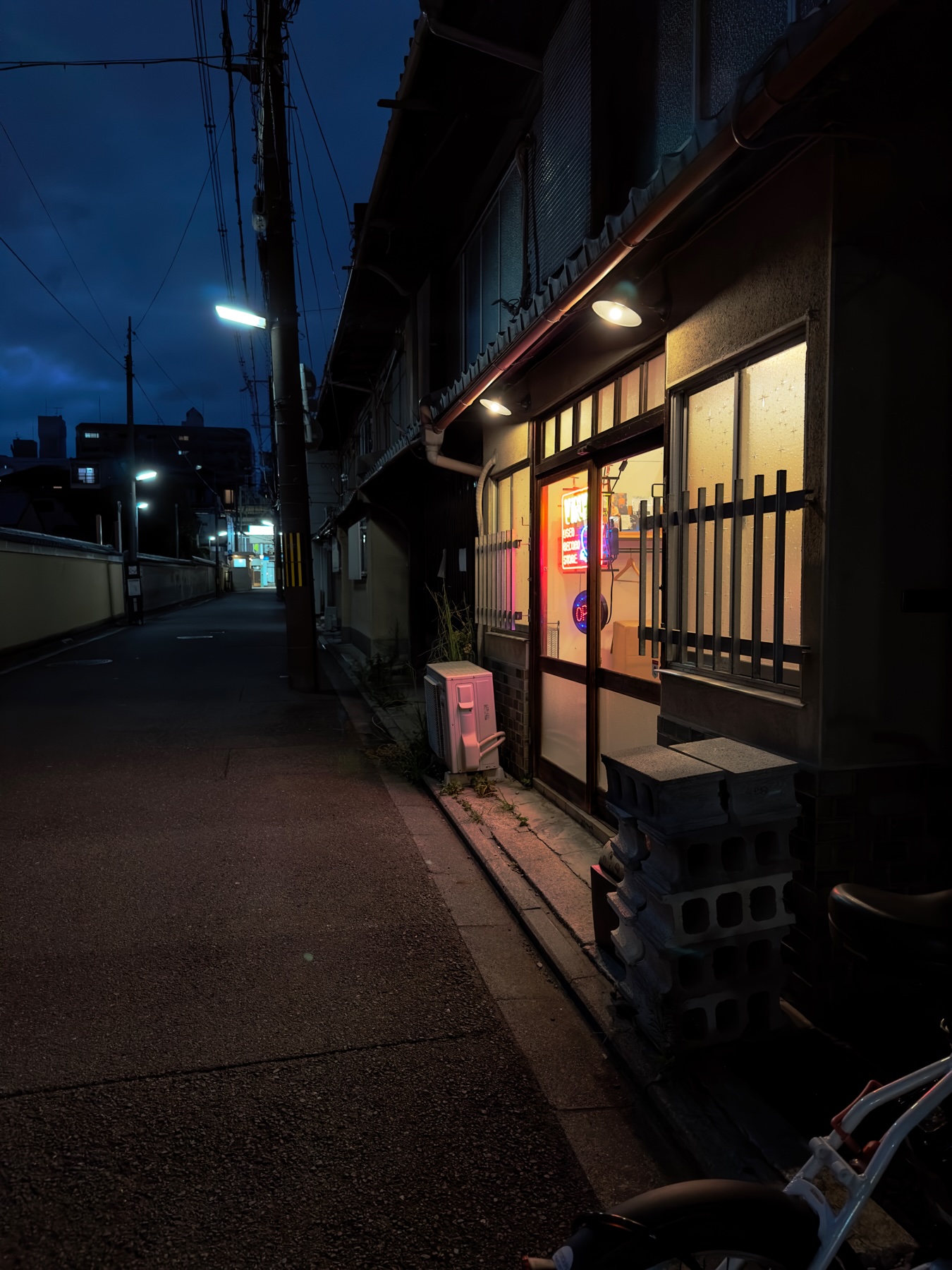 A dark Kyoto alley with the neon of a store lighting yellow into the blues of the night