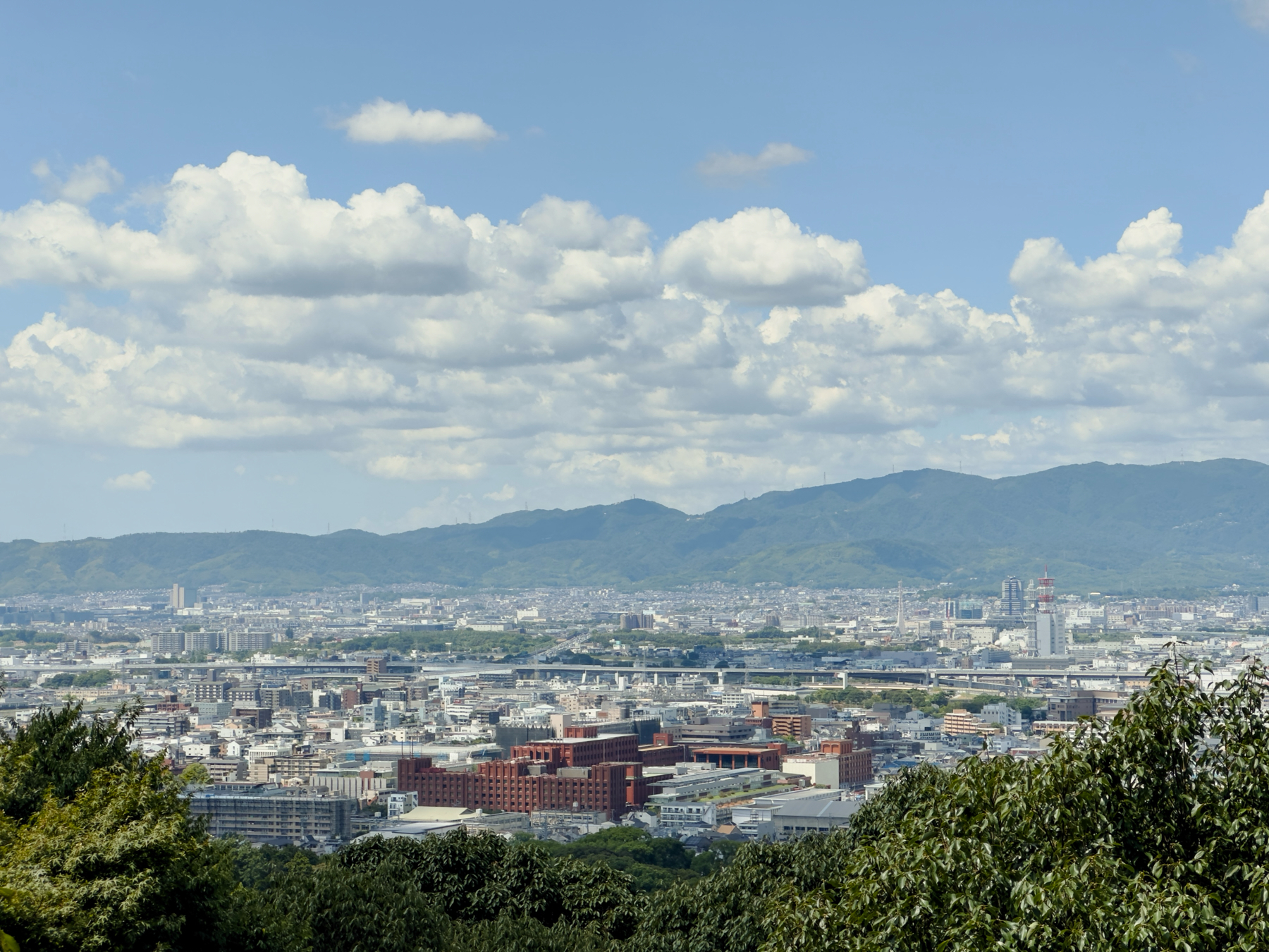 A view over Kyoto from halfway up the trail. The entire city and the lush green hills can be seen in the background.