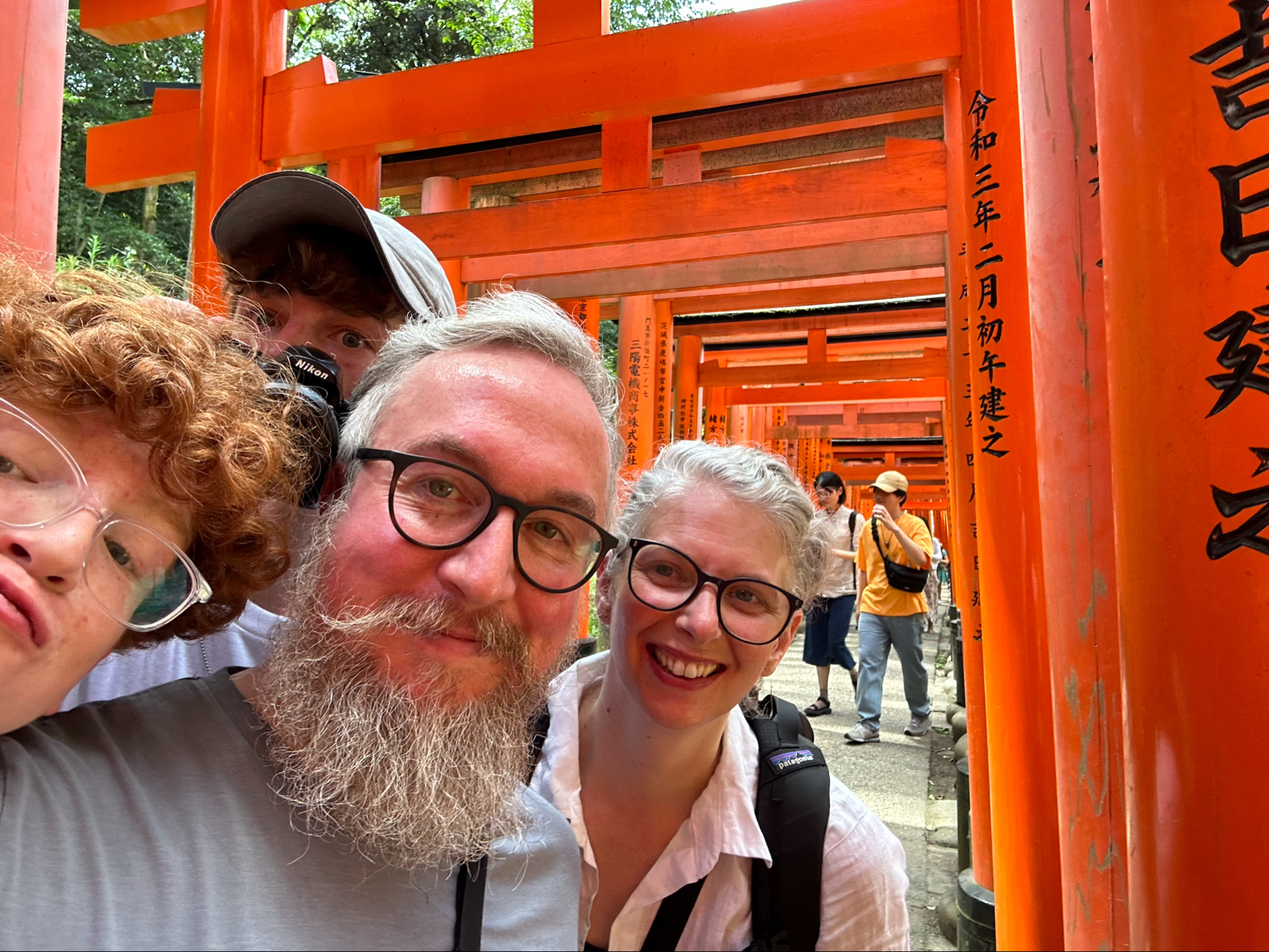 The whole family taking a selfie in front of vibrant orange torii gates at Fushimi Inari Shrine in Kyoto, Japan.