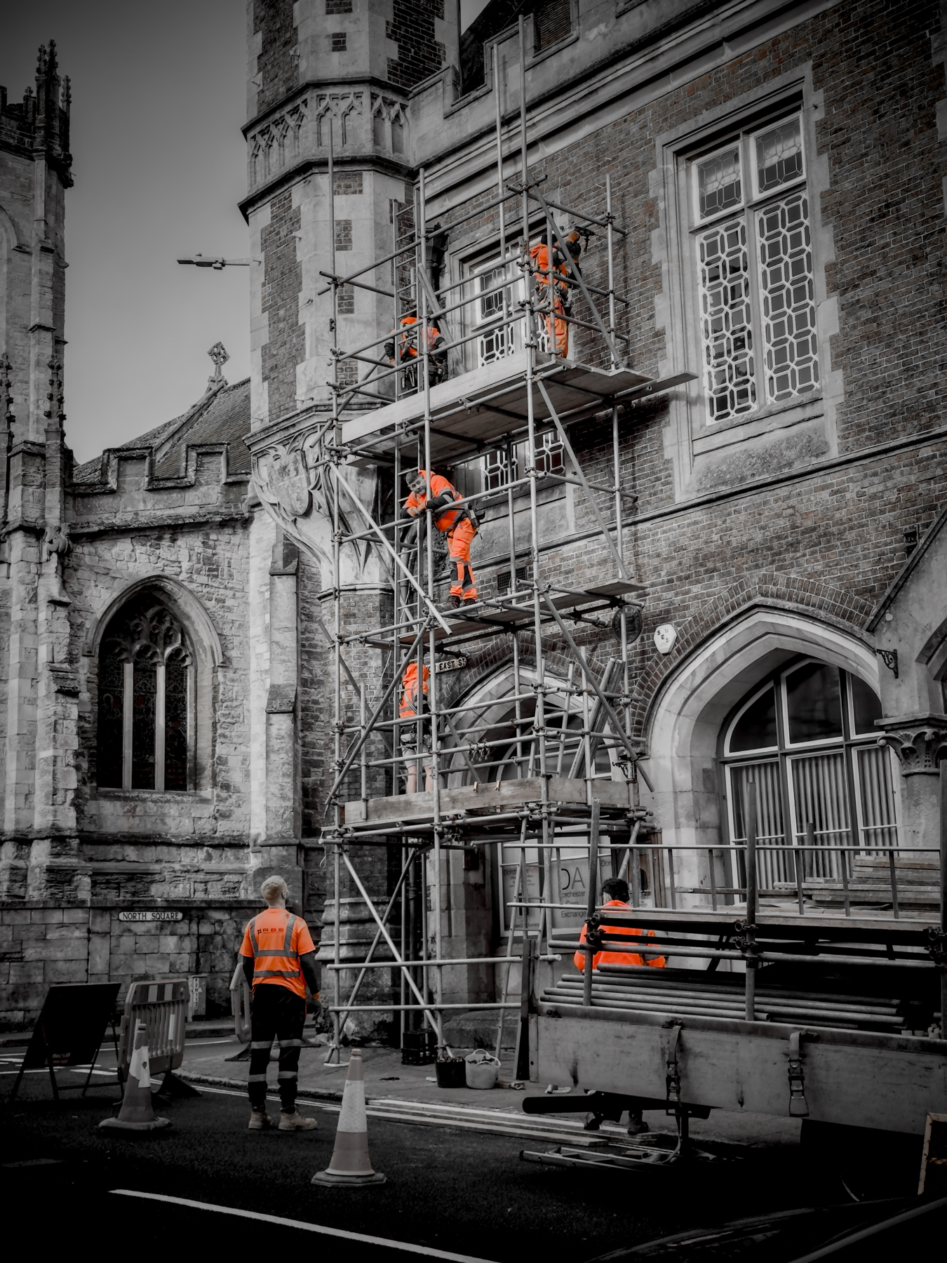 Construction workers in high visibility clothing assembling scaffolding beside a historic building.