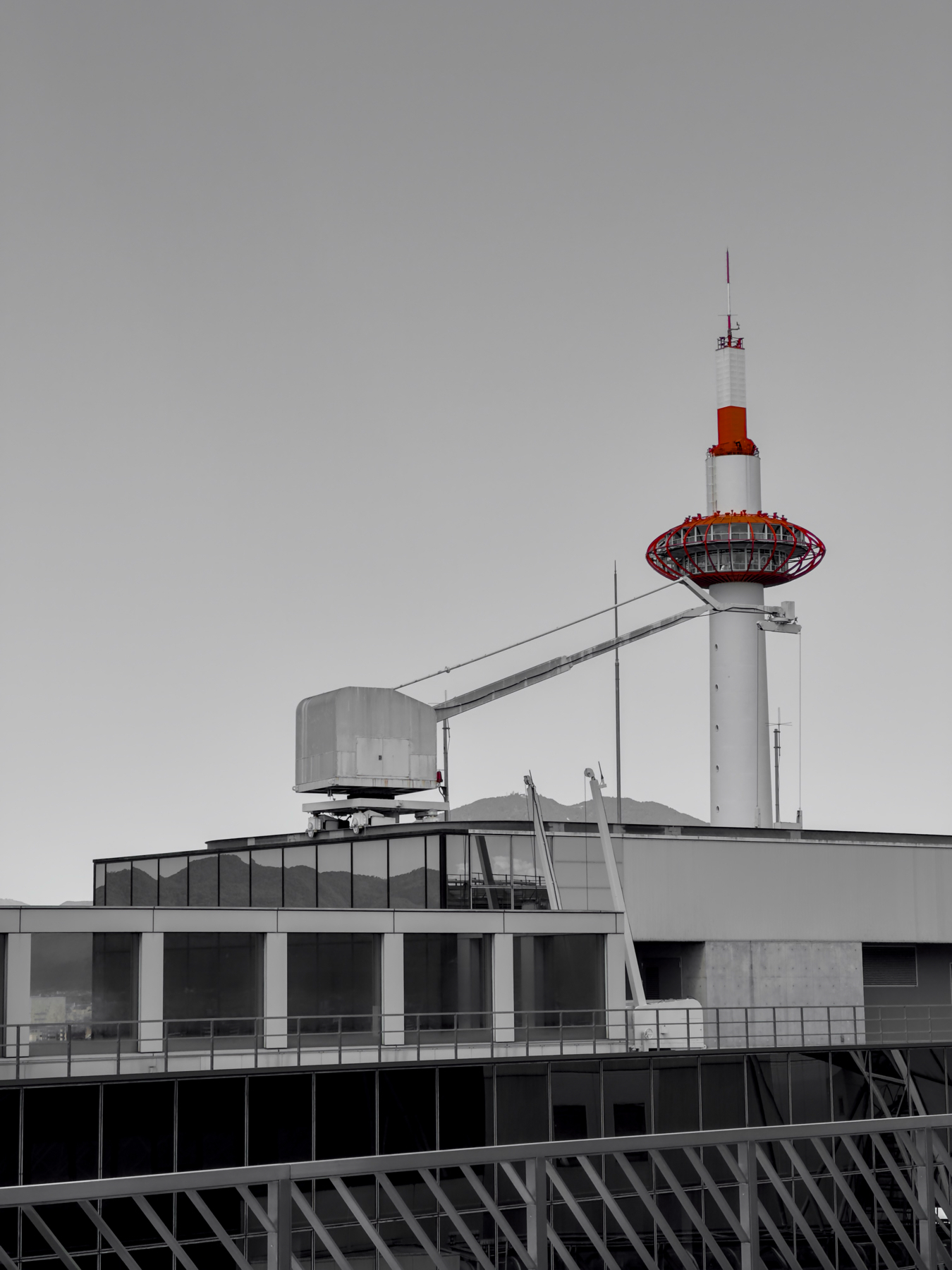 A black and white image featuring a Kyoto Tower in the background with geometric structures in the foreground. Red has been selectively kept in the image