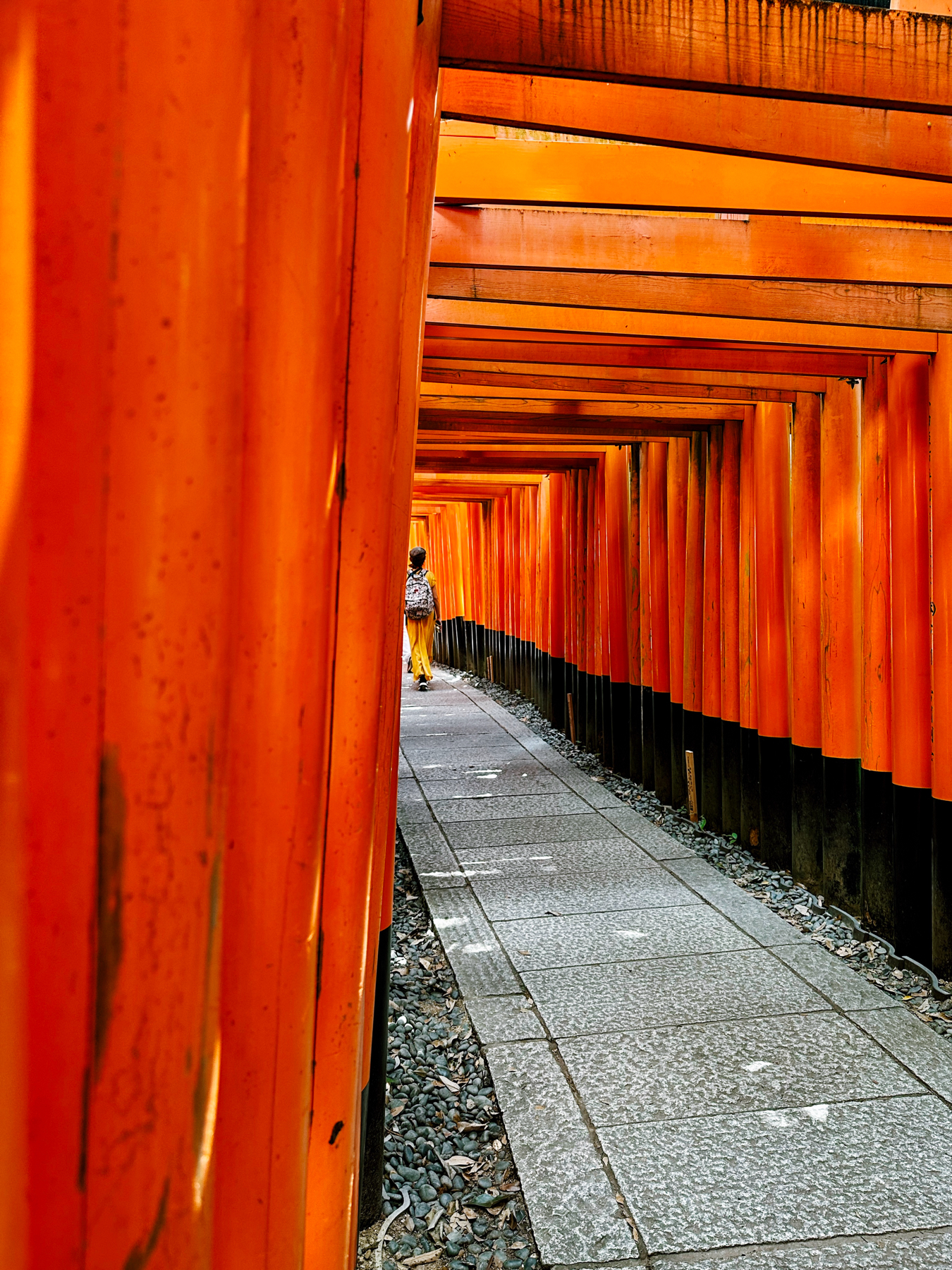 Pathway flanked by vibrant orange torii gates with a person in the background at Fushimi Inari Shrine in Kyoto, Japan.