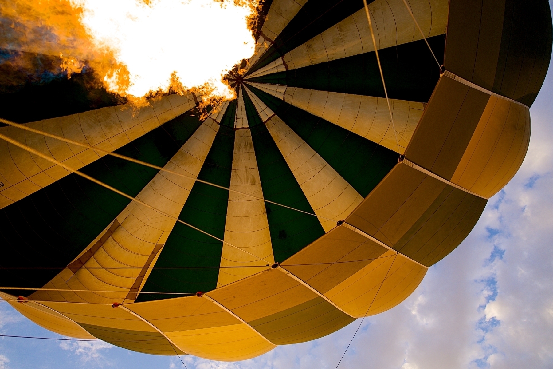 A photo taken up showing the inside of a ballon against the sky. A flame is burning.