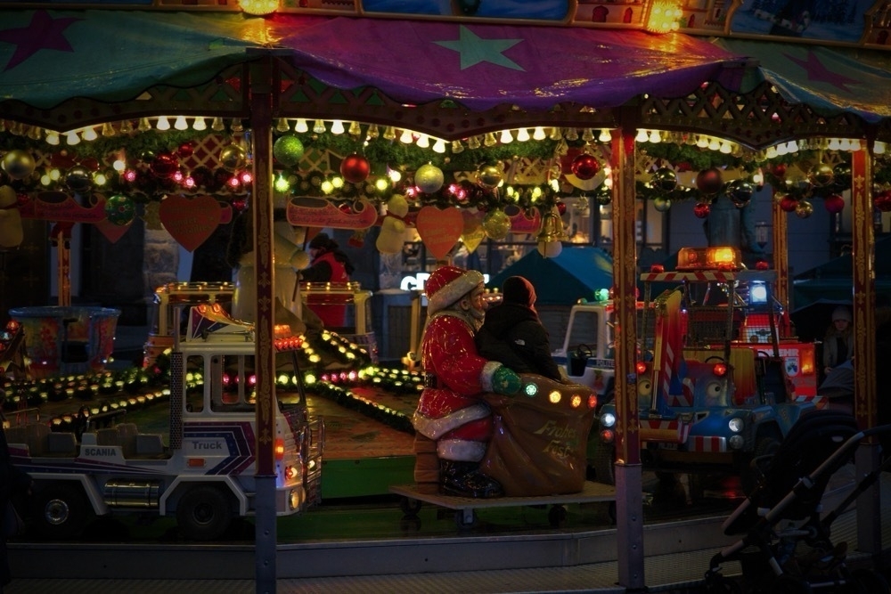 A Christmas themed carousel. A person with a cap sitting in front of Santa clause on the ride.