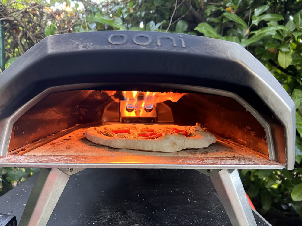A pizza is baking under orange flames. 