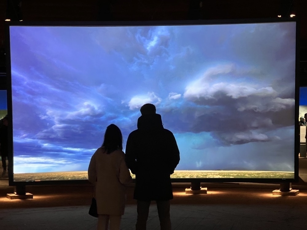 two persons in front of a projected image of clouds