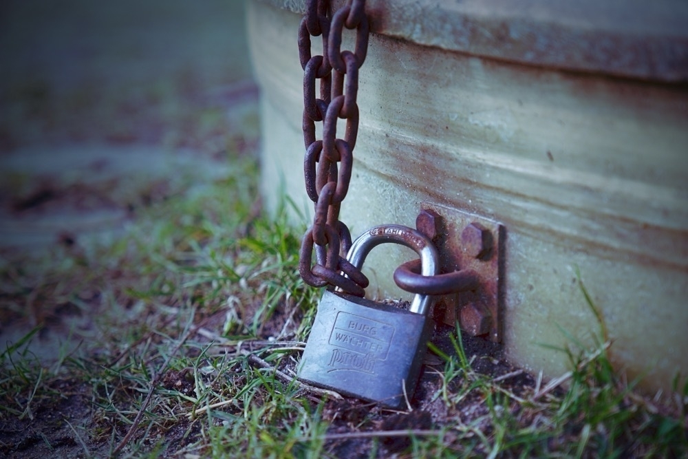 A lock and a rusty key securing a container on some muddy grass