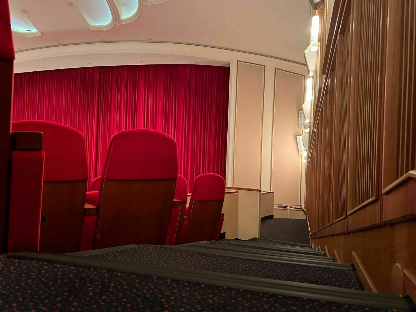 A cinema with a closed curtain, red seats in the foreground.