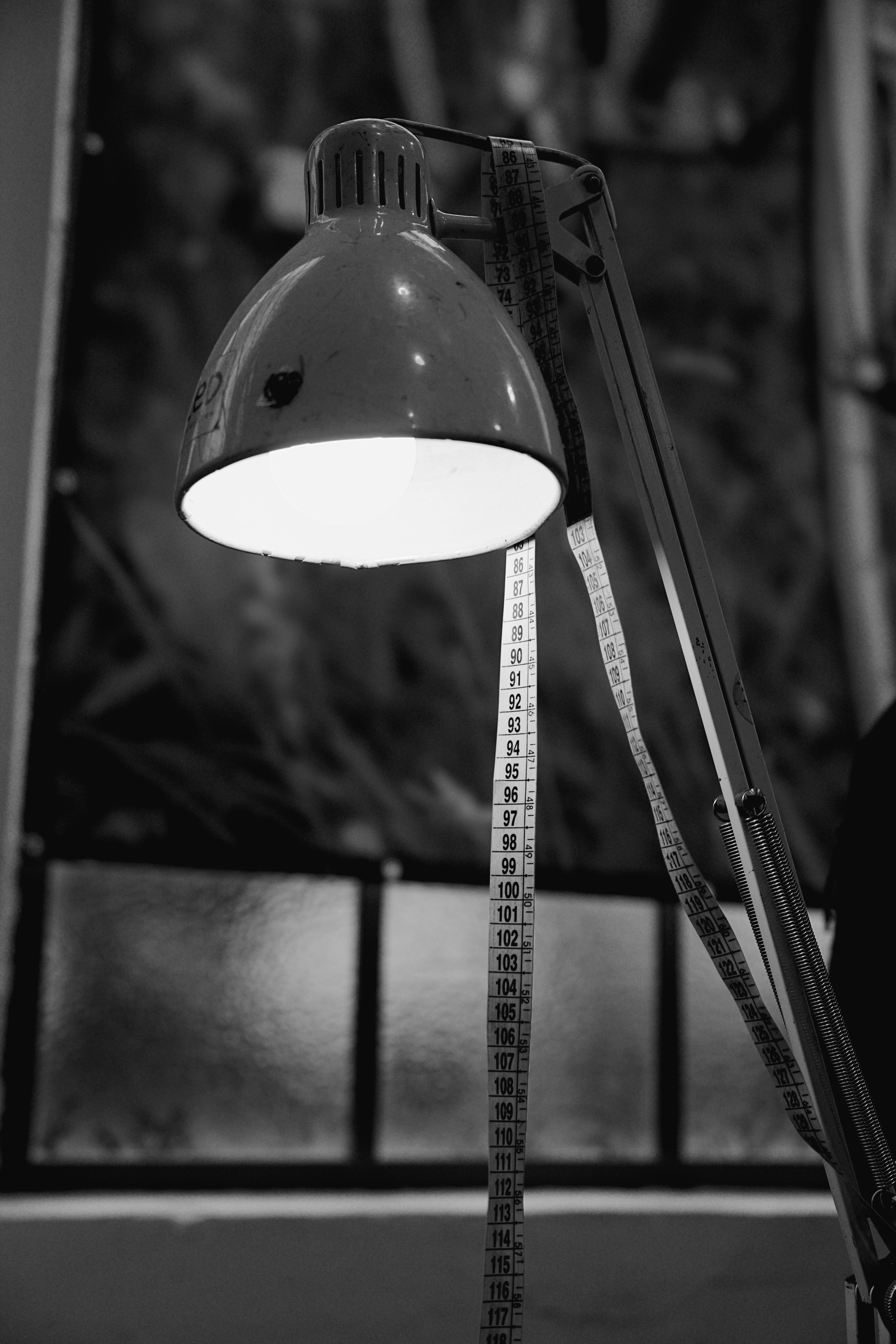 A black and white image of a desk lamp, a tape meassure around it.
